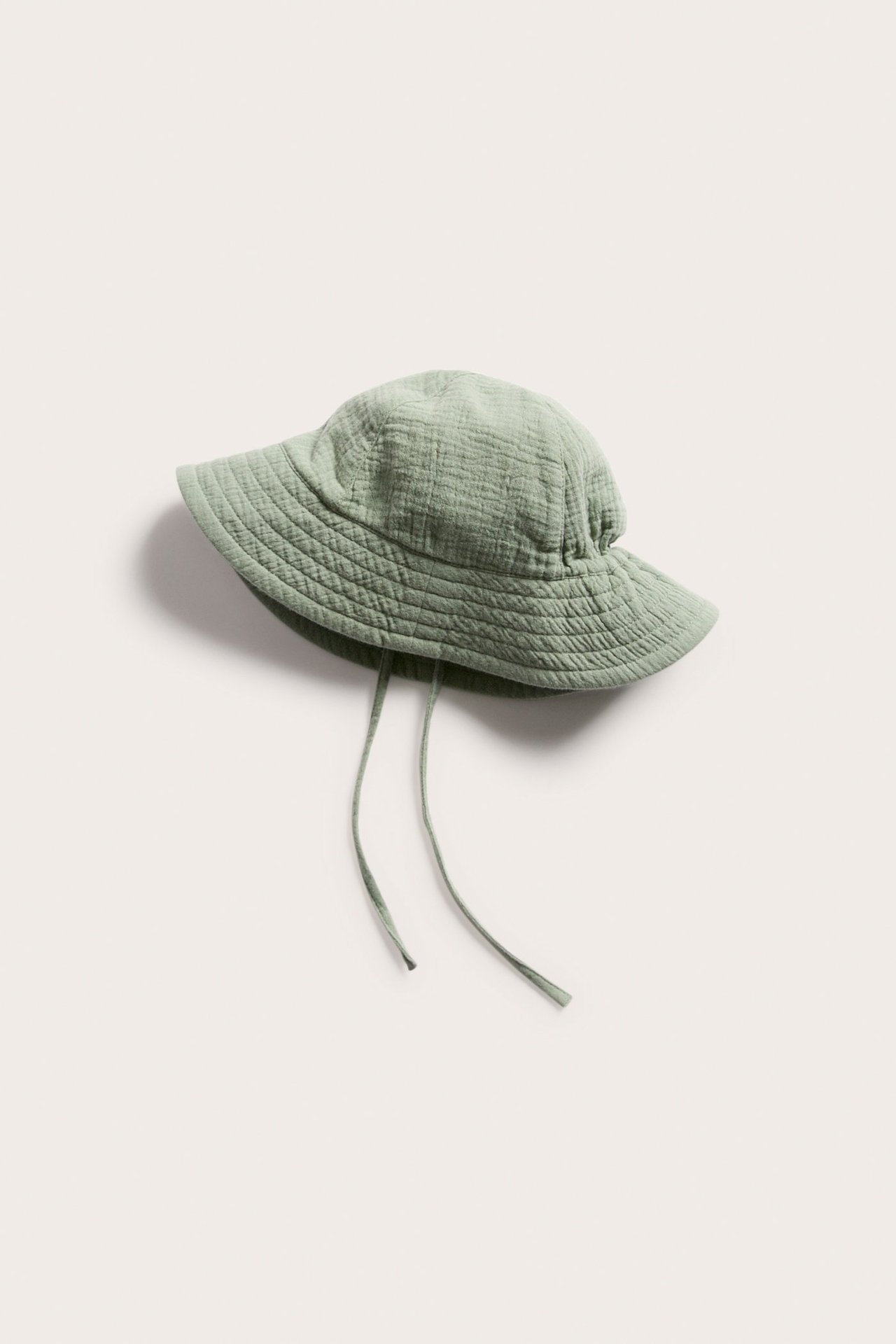 Edestäpäin kuvattu tummanvihreä, rypistetty puuvillainen vauvan aurinkohattu leveällä lierillä ja solmimisnauhoilla.