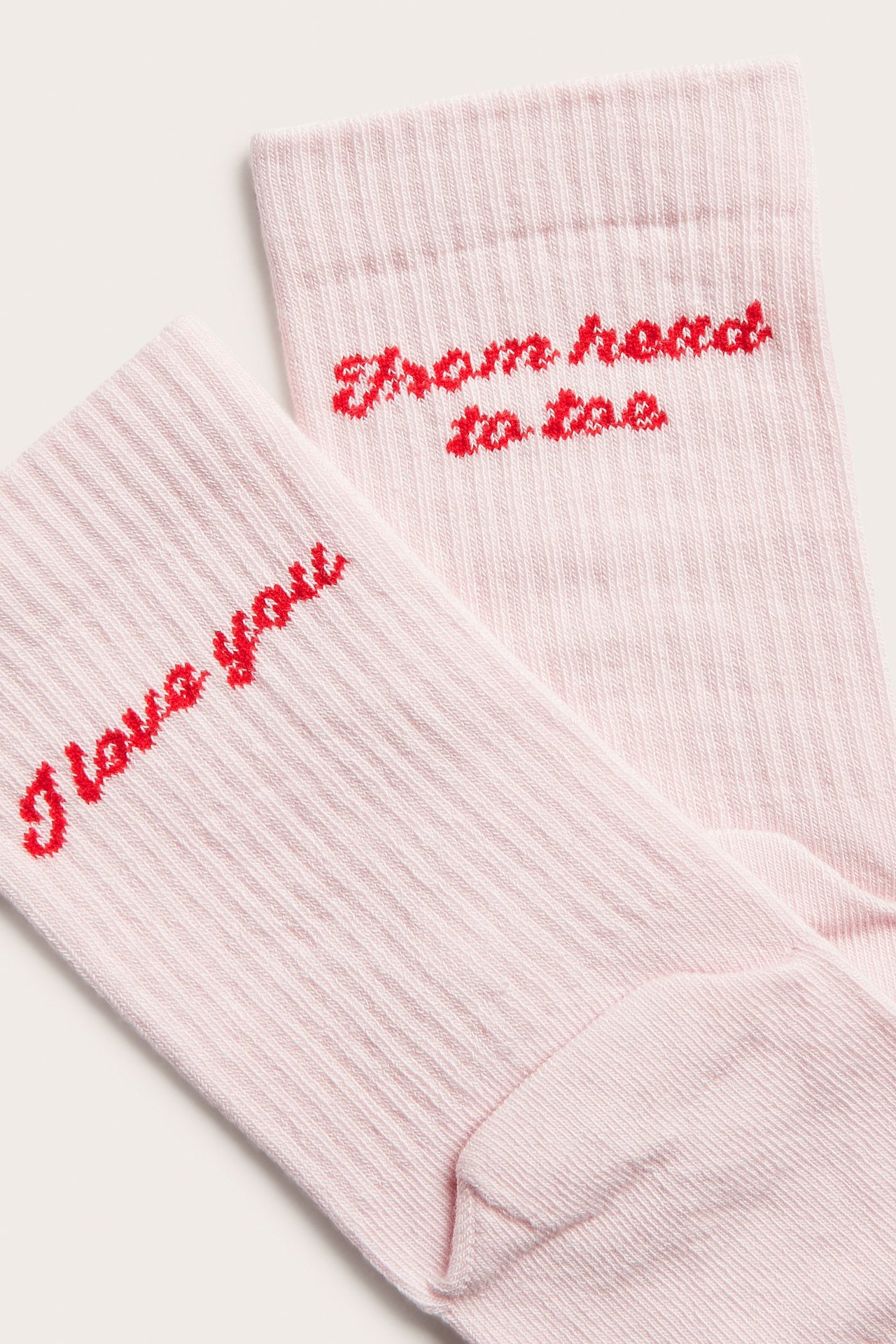 Lähikuva kahdesta vaaleanpunaisesta ribatusta sukasta punaisella brodeeratulla tekstillä: "I love you" ja "From head to toe".