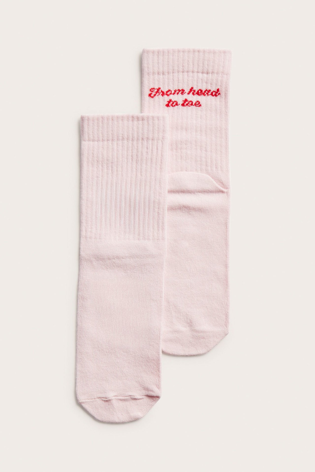 Edestä näkymä kahdesta vaaleanpunaisesta ribbineulossukasta, joissa on punaisella kirjailtu teksti "From head to toe".