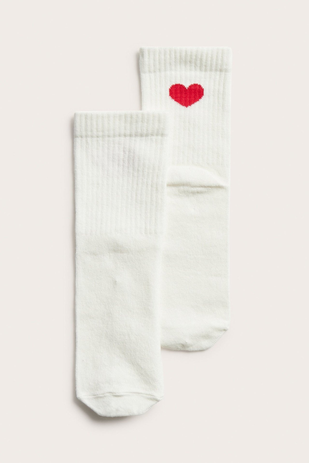 Ylhäältä näkymä, pariskunta luonnonvalkoisia resorisukkia, toisessa punainen sydänkuvio varressa.