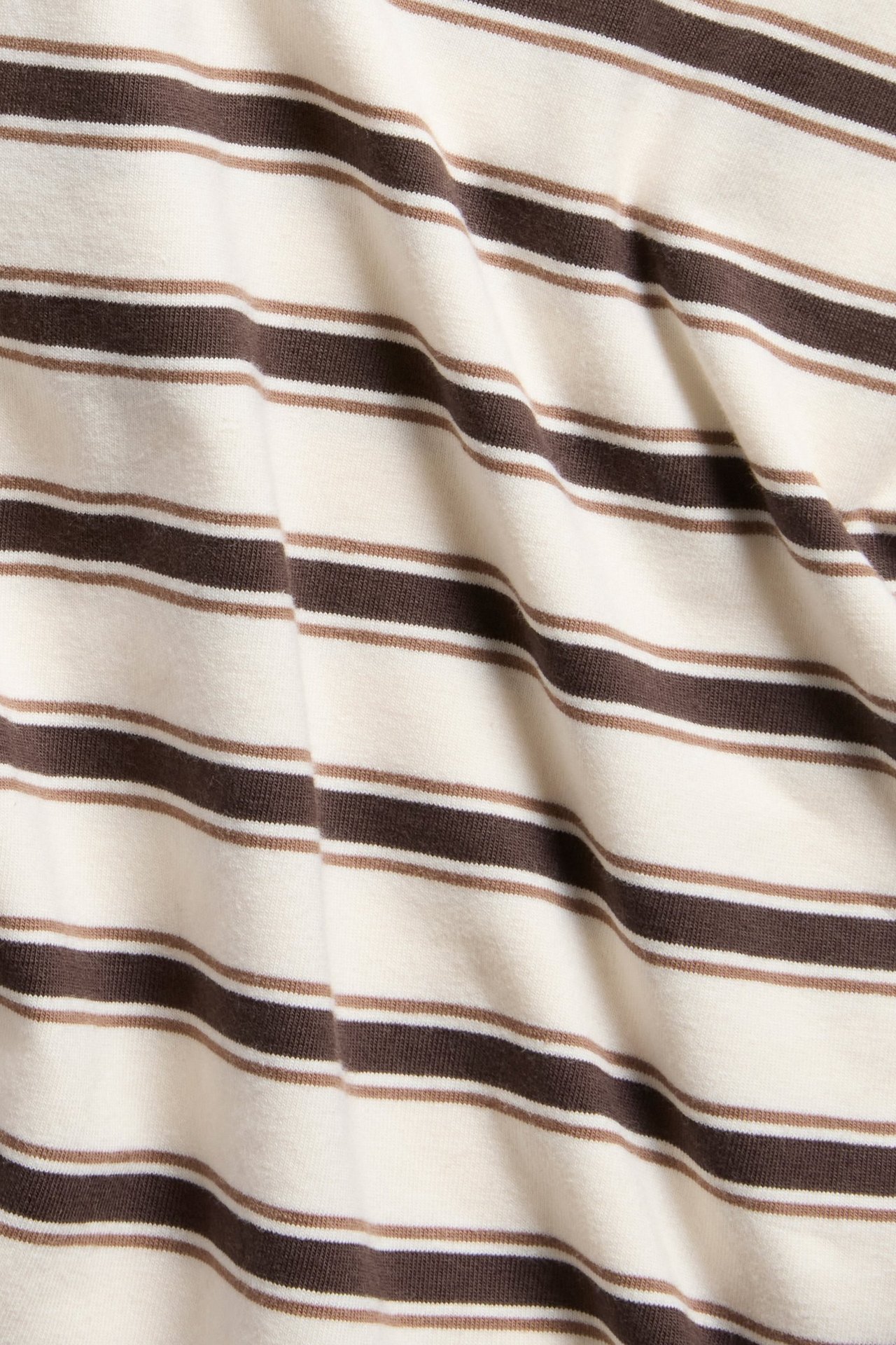 Zbliżenie na dopasowany T-shirt w kolorze złamanej bieli, z ciemnymi i jasnymi brązowymi poziomymi paskami.