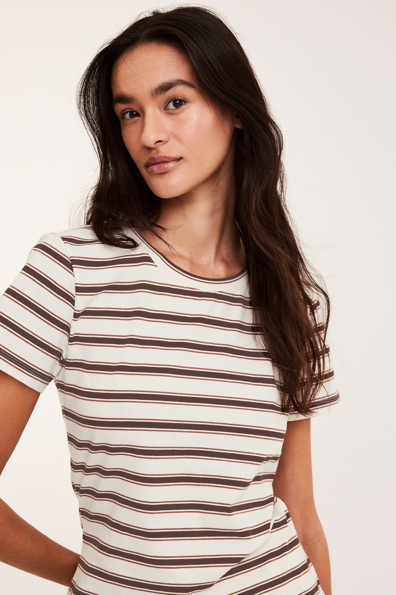 Frontbilde av kvinne i tettsittende off-white stripete t-skjorte med brune striper og rund hals.