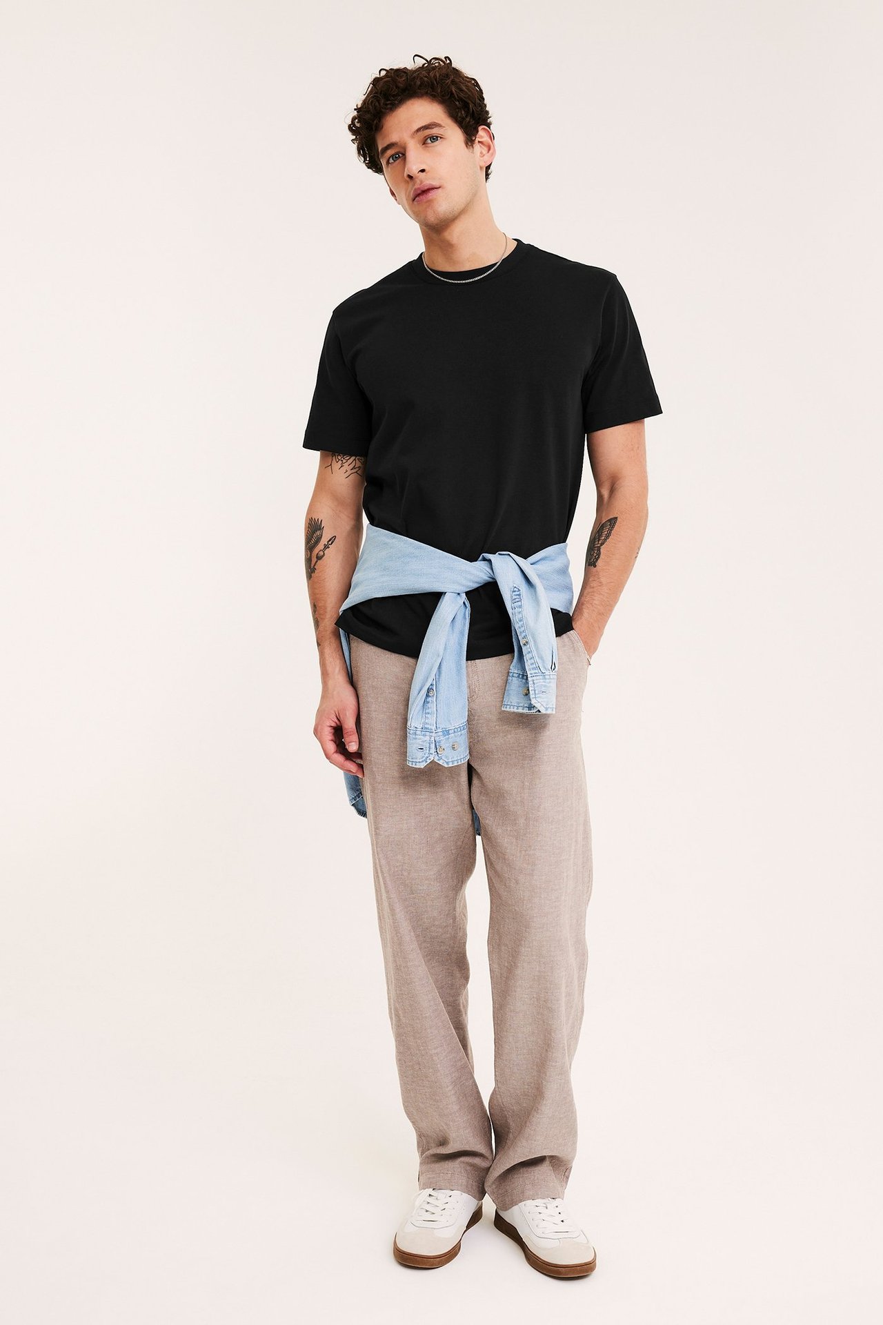 Frontbilde: Mann i svart løs t-skjorte, beige bukser, hvite joggesko. Lys blå dongeriskjorte knyttet i midjen.