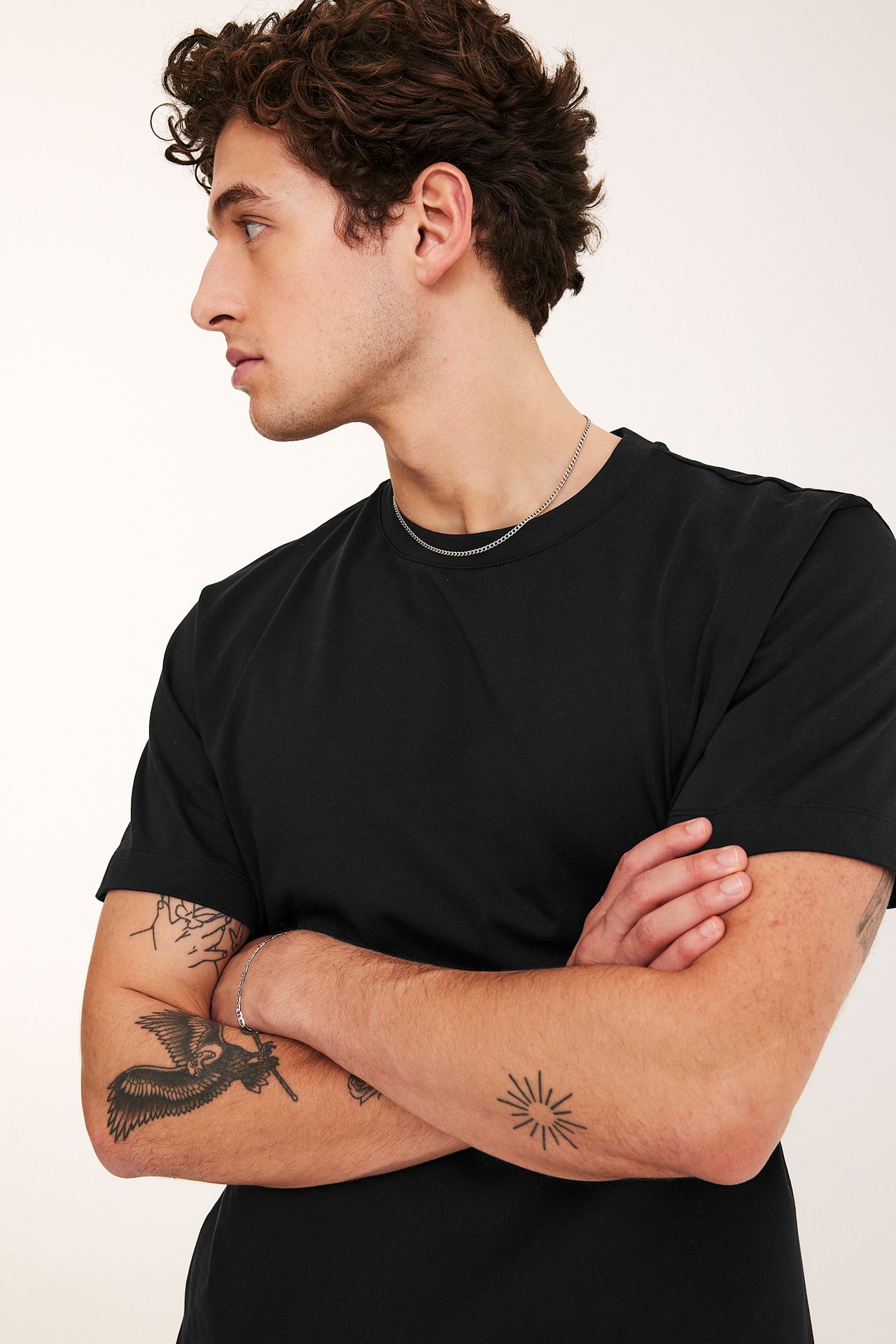 Widok z boku mężczyzny w czarnym, luźnym bawełnianym T-shircie, srebrnym łańcuszku i bransoletce.