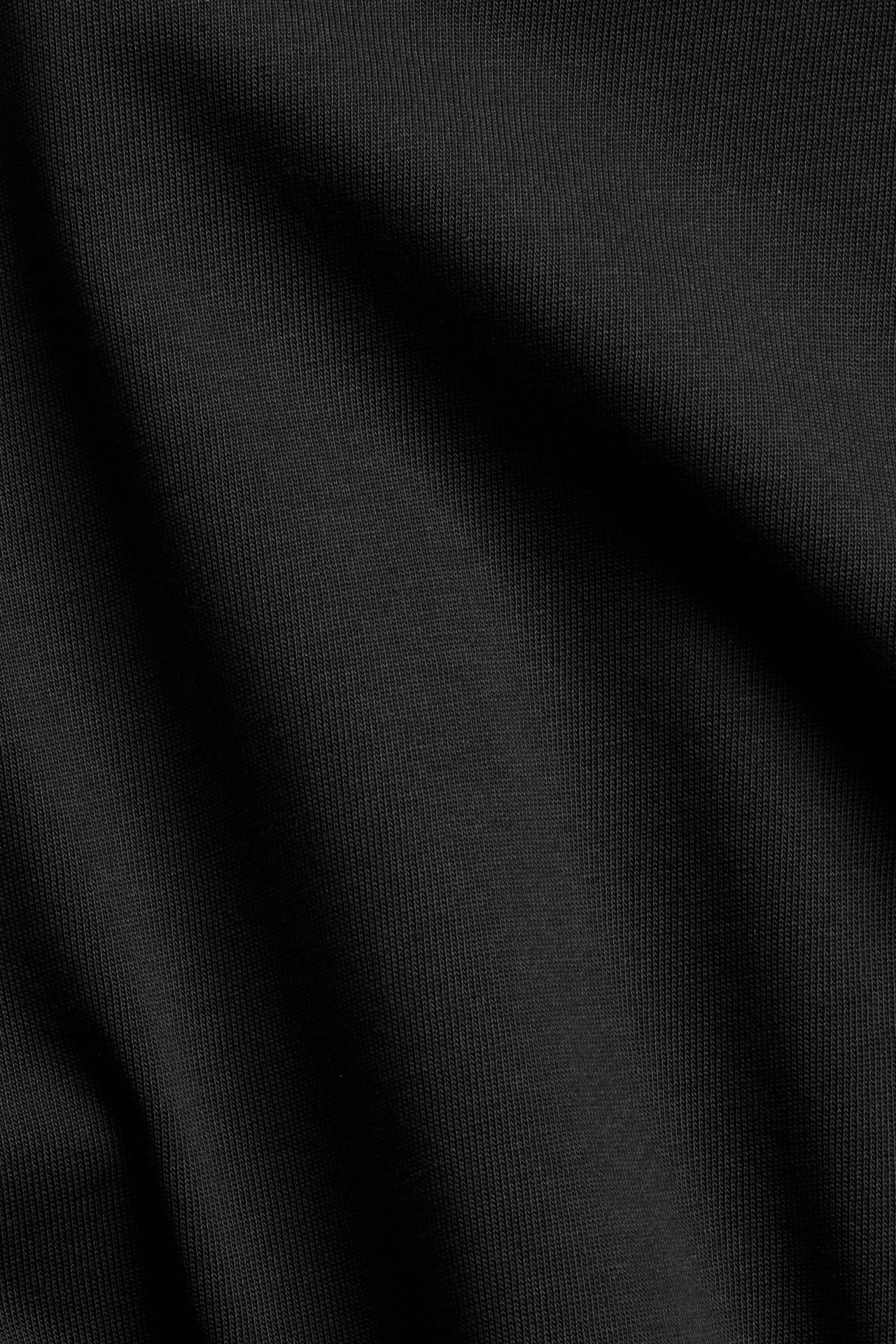 Närbild på ett svart enfärgat tyg från en T-shirt i bomull, med diskreta veck.