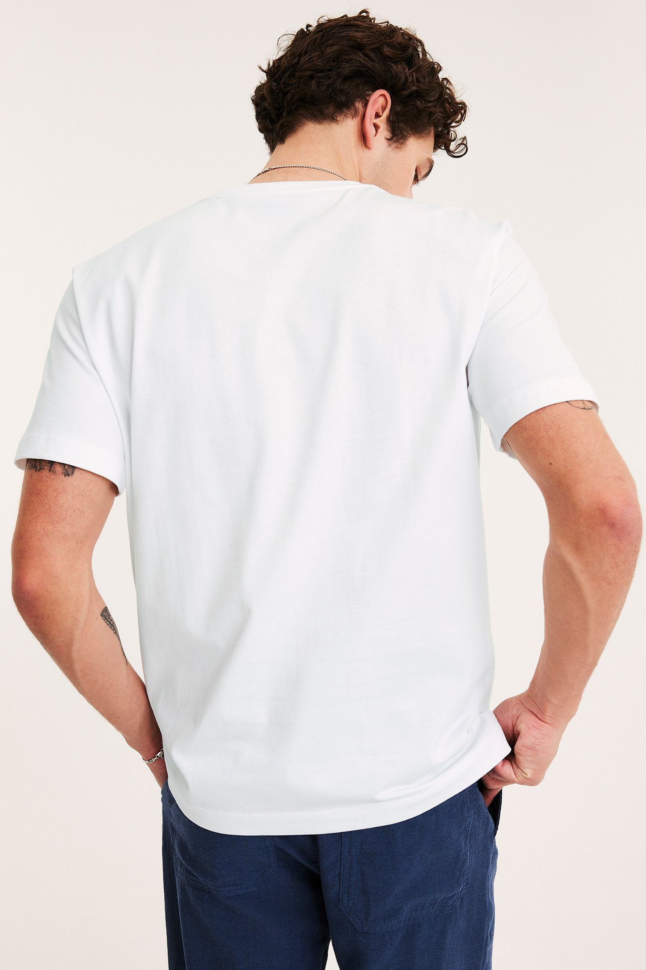 Mężczyzna od tyłu w białym, luźnym bawełnianym t-shircie, niebieskich spodniach i srebrnej bransoletce.