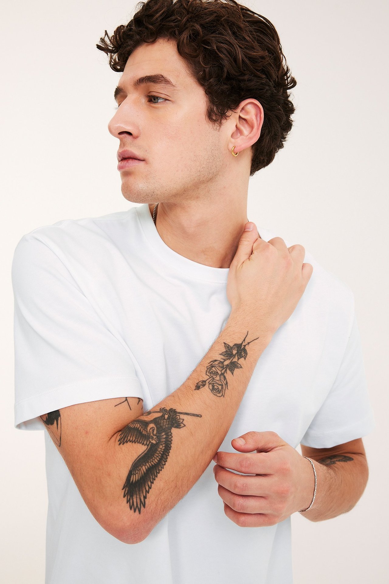 Zbliżenie z boku mężczyzny w białym, luźnym t-shircie, srebrnej bransoletce i złotym kolczyku.