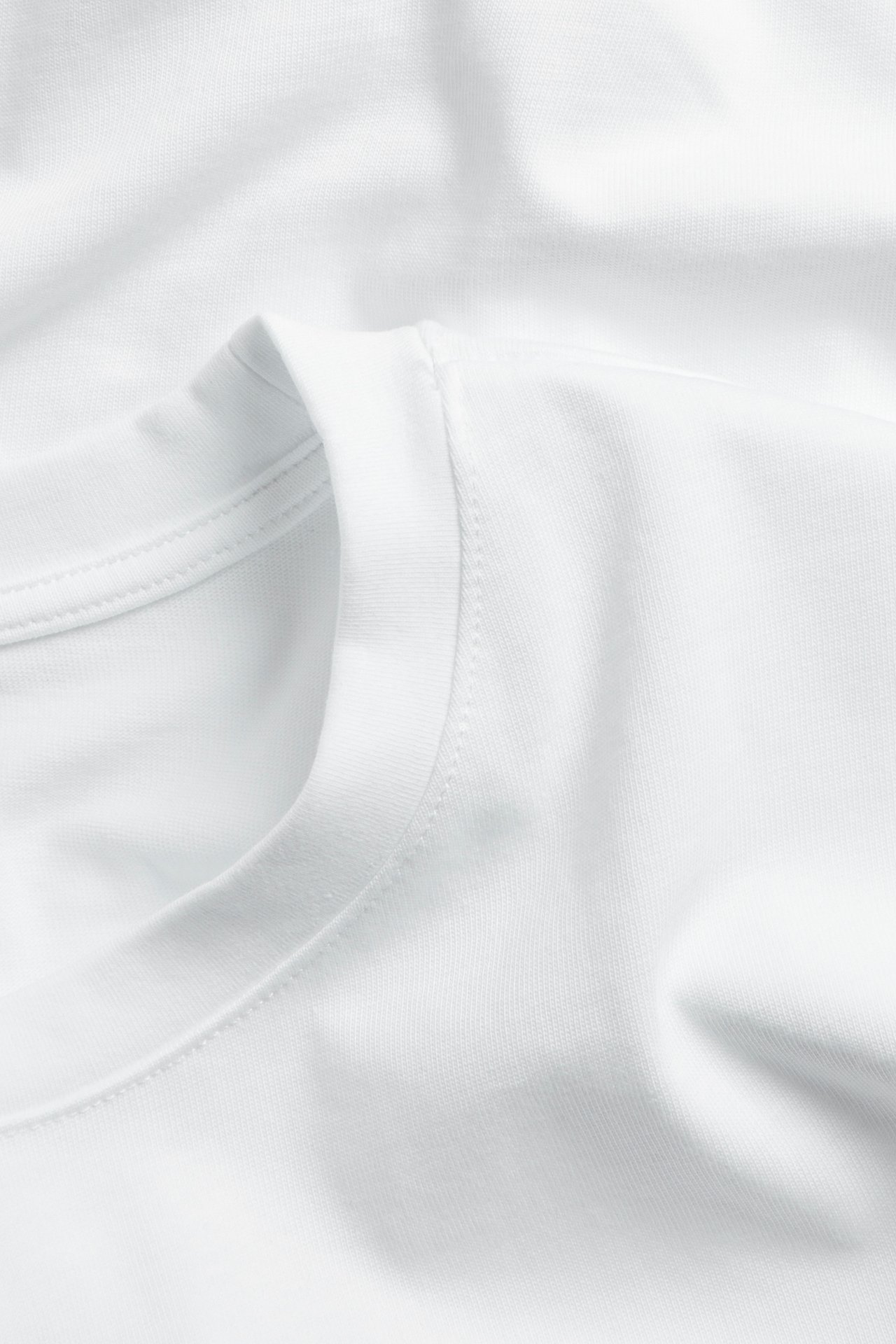 Nærbilde av en hvit, løs bomulls-T-skjorte med rund hals, som viser den ribbestrikkede halskanten.