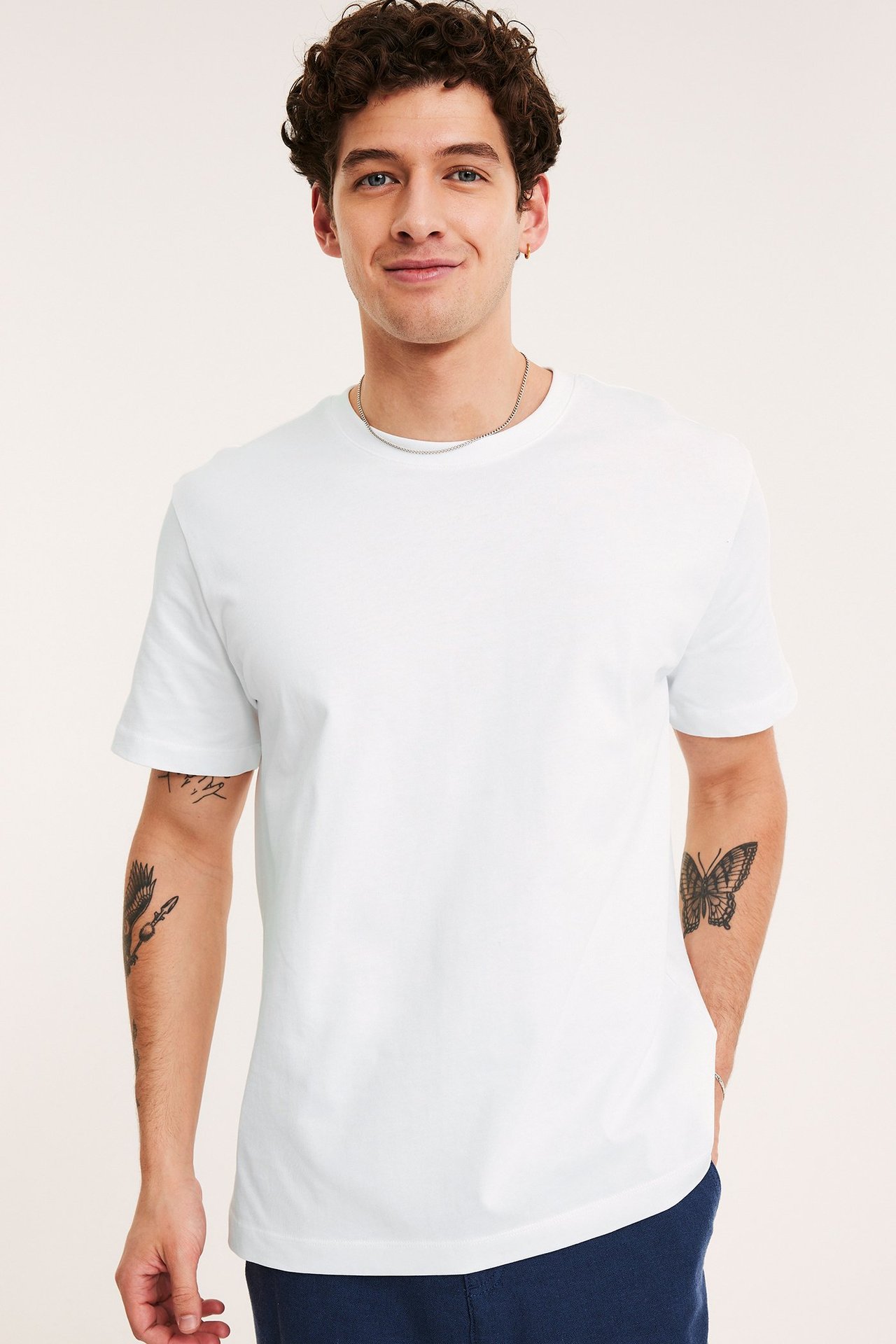 Frontvisning: Mann i hvit løs O-hals bomulls-T-skjorte, sølvkjede og mørkeblå bukse.
