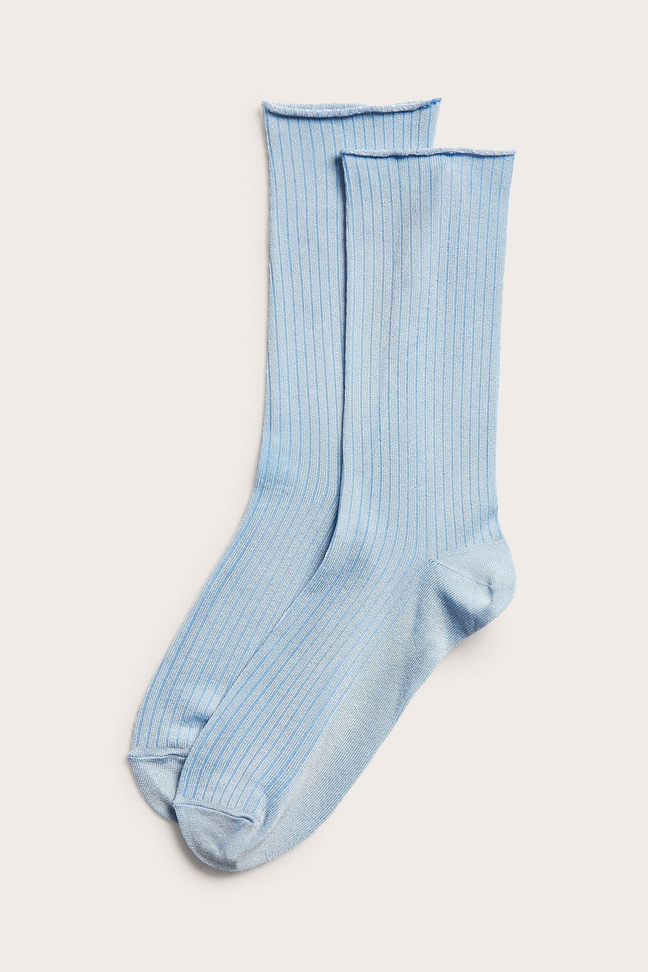 Kaksi vaaleansinistä, uurrettua, kiiltävää sukkaa rullareunalla, aseteltuna edestä päin.