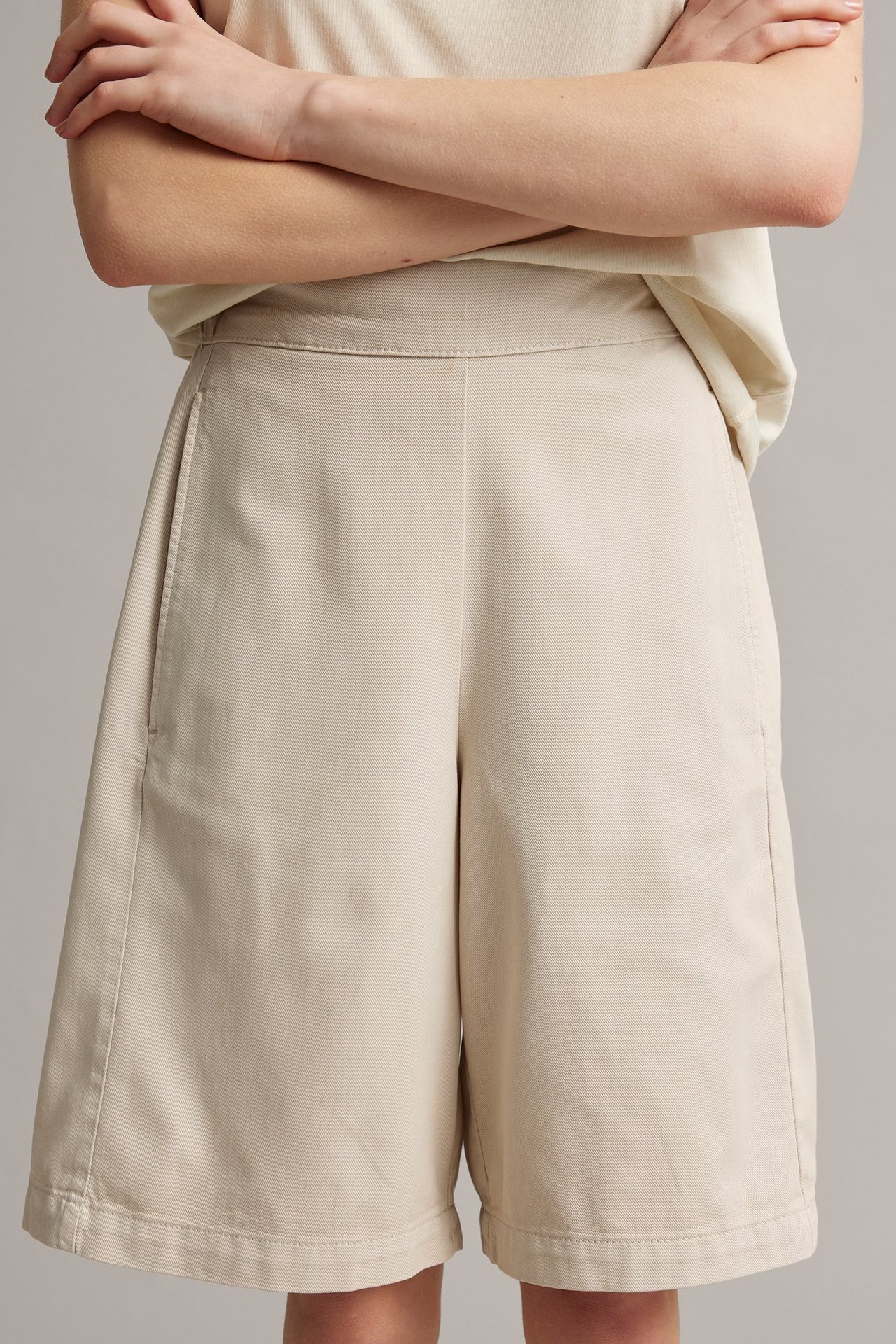 Frontbilde: kvinne i lysebeige, vide bermudashorts med sidelommer og en lys topp.