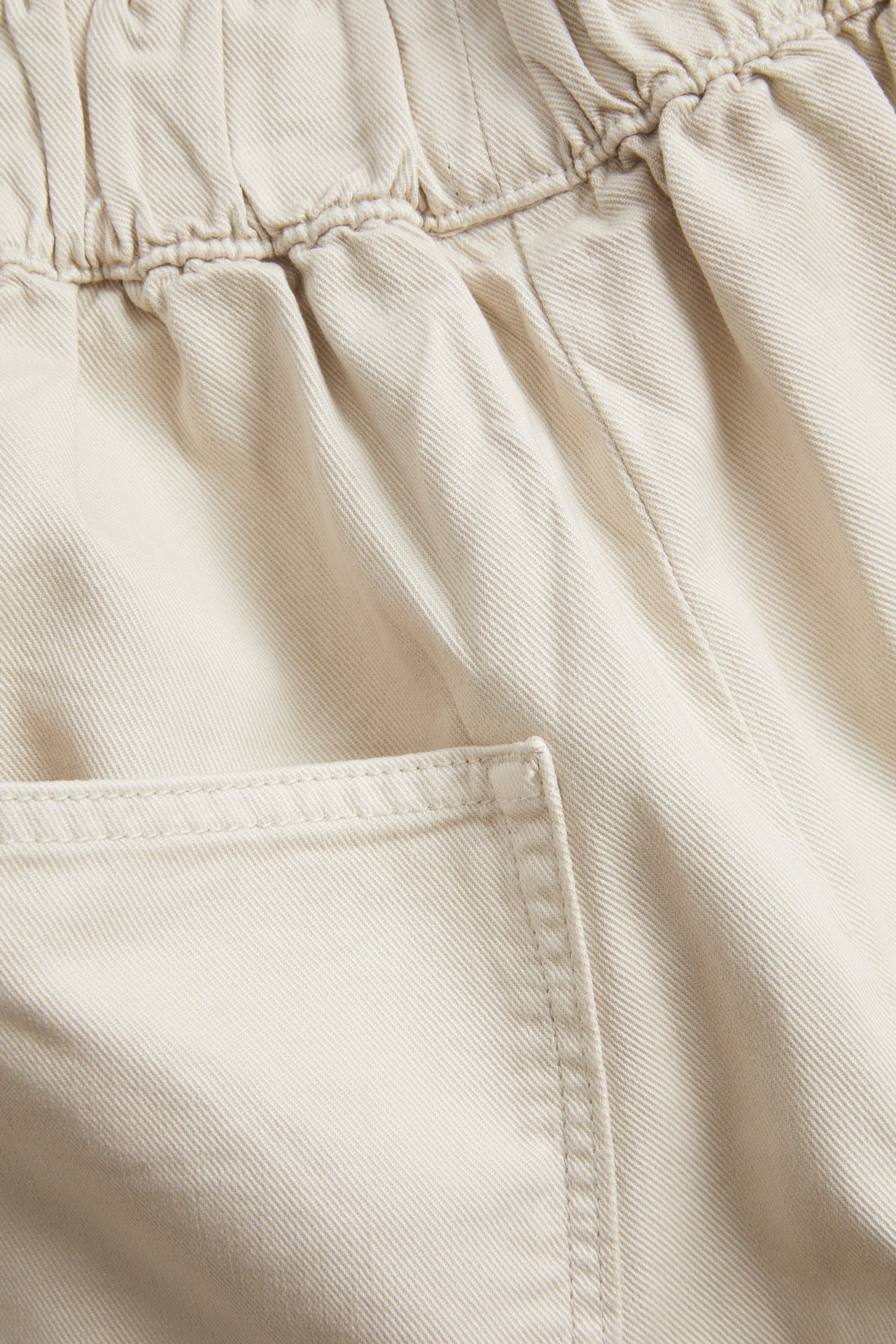 Lähikuva vaaleanbeigestä puuvillasekoite bermudashortsista, jossa joustava vyötärö ja sivutasku.