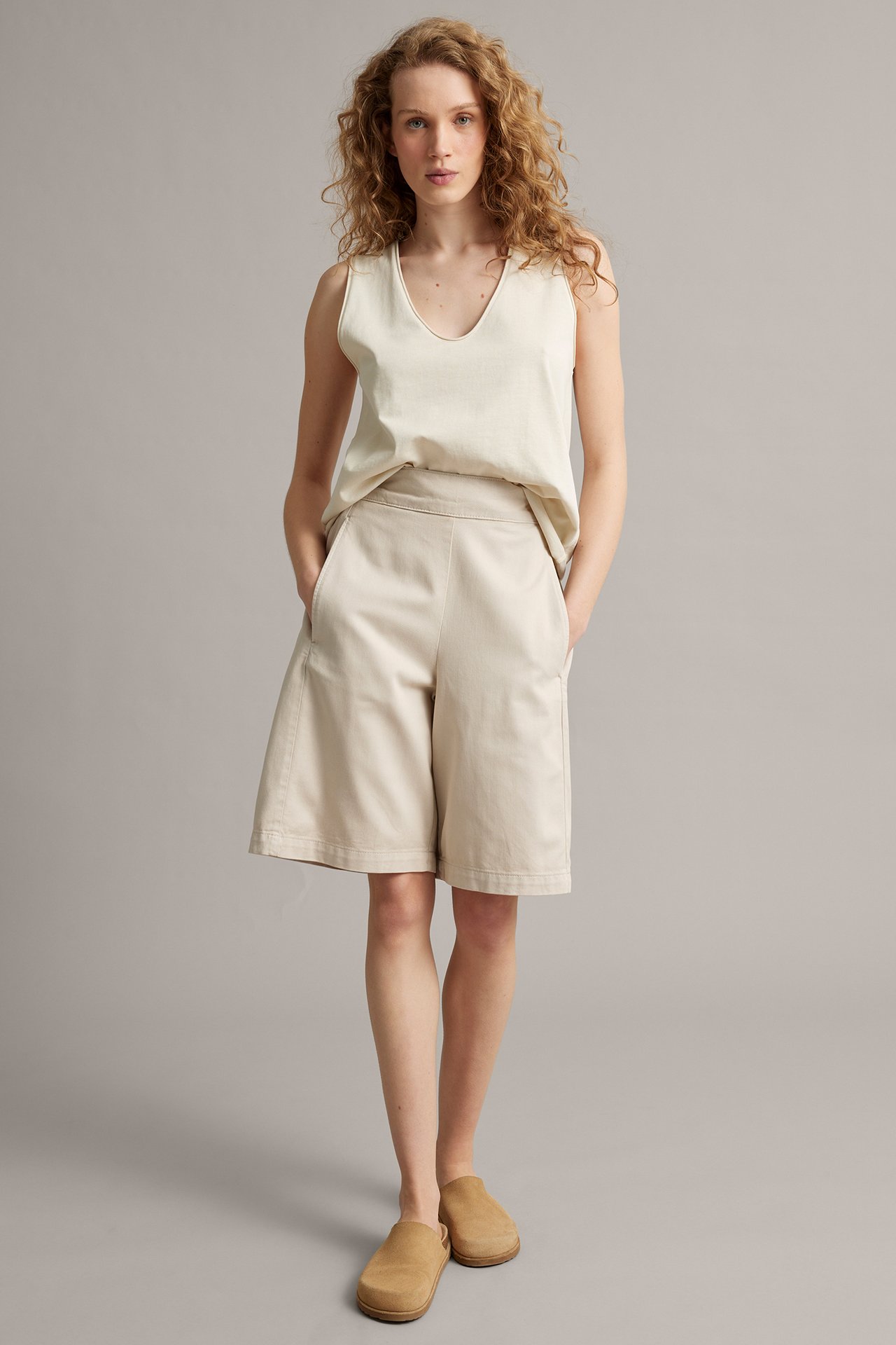 Widok z przodu: Kobieta w jasnobeżowych lyocell-bawełnianych szortach bermudach, jasnobeżowym topie i jasnobrązowych klapkach.