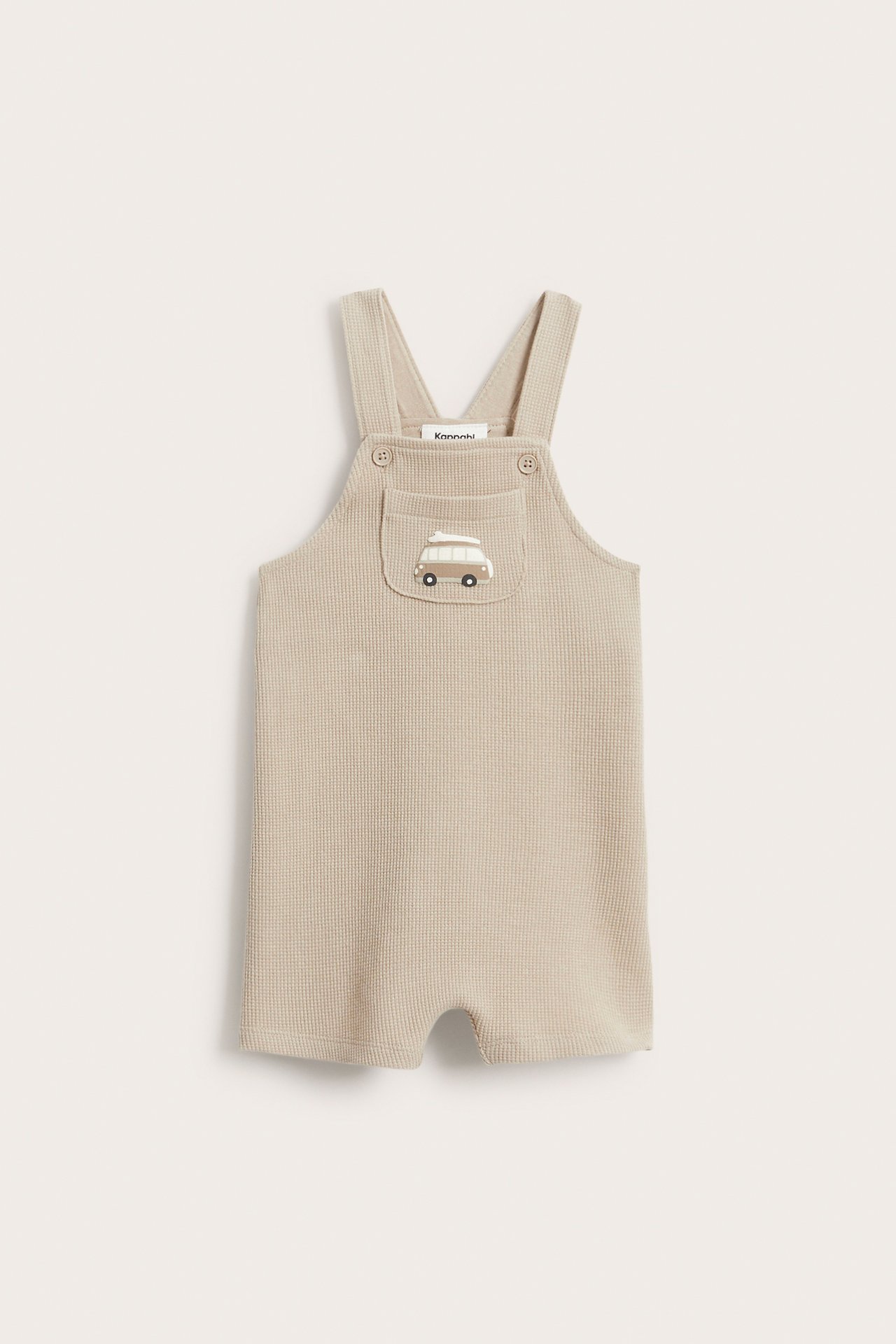 Widok z przodu beżowych waflowych ogrodniczek niemowlęcych z guzikami i kieszonką z haftowanym vanem.