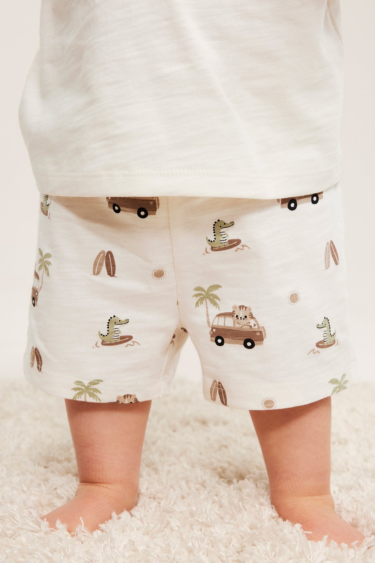 Frontvy av baby i benvita djurmönstrade jersey-shorts och en benvit t-shirt.