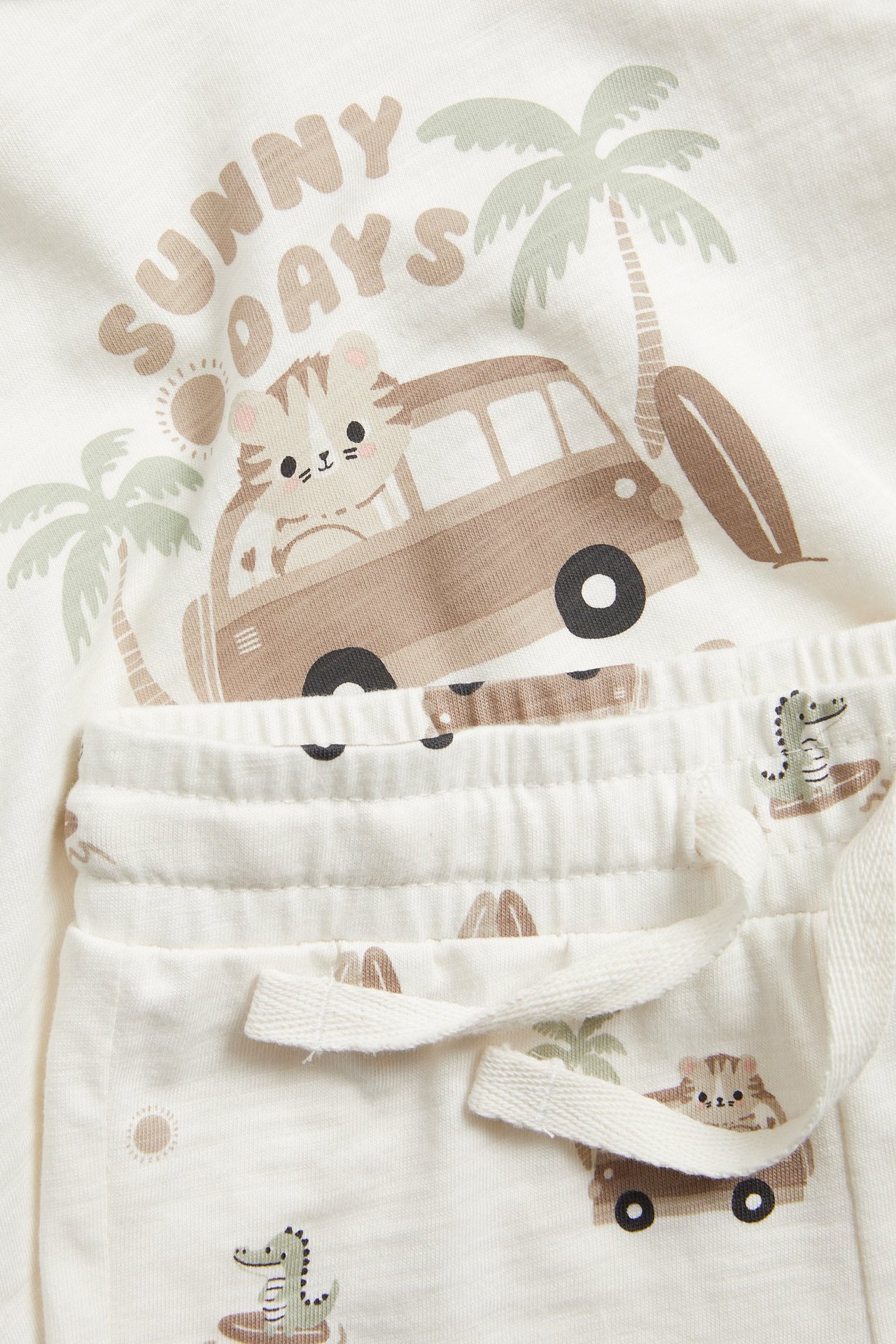 Närbild av ett benvitt baby-set i jersey med t-shirt och shorts med lekfullt sommartryck.