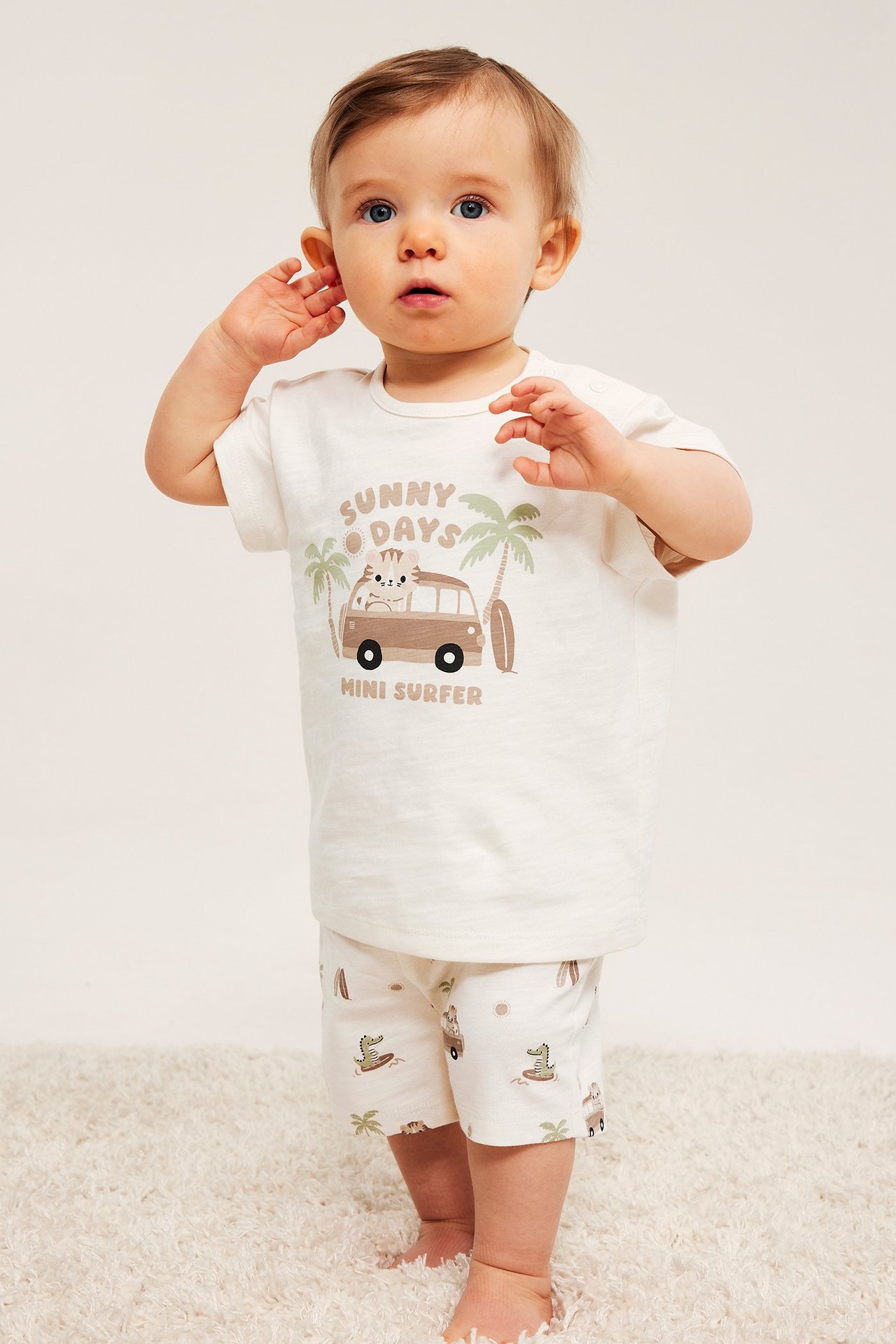 Widok z przodu: niemowlę w ecru bawełnianym zestawie: koszulka z nadrukiem i wzorzyste szorty.