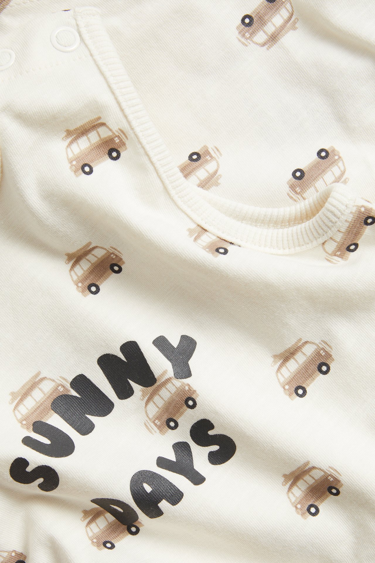 Lähikuva luonnonvalkoisesta vauvan collegehaalarista, ruskea bussikuvio, "SUNNY DAYS" teksti, nepparit.