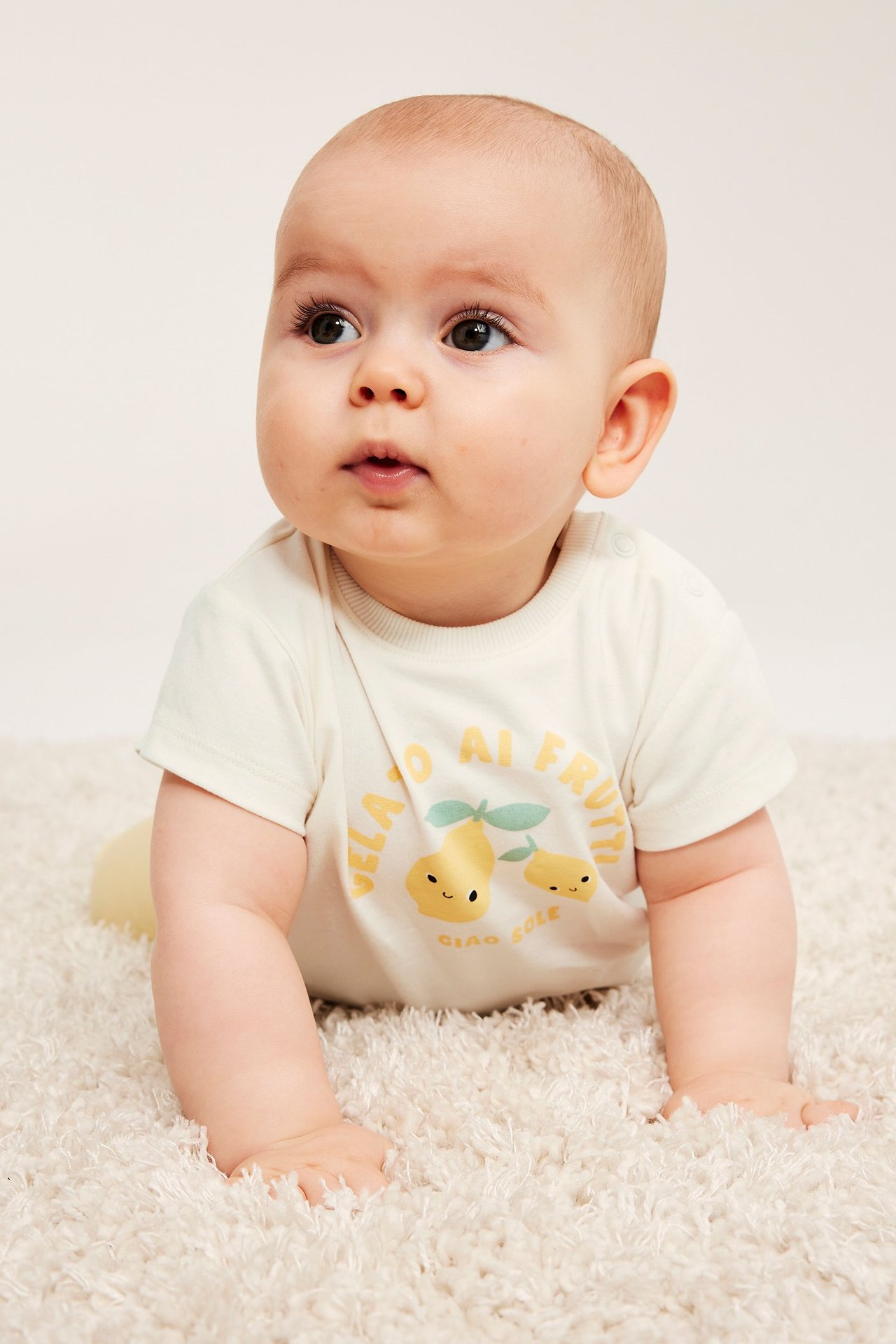 Widok z przodu niemowlęcia w kremowym t-shircie z kolorowym nadrukiem owoców.