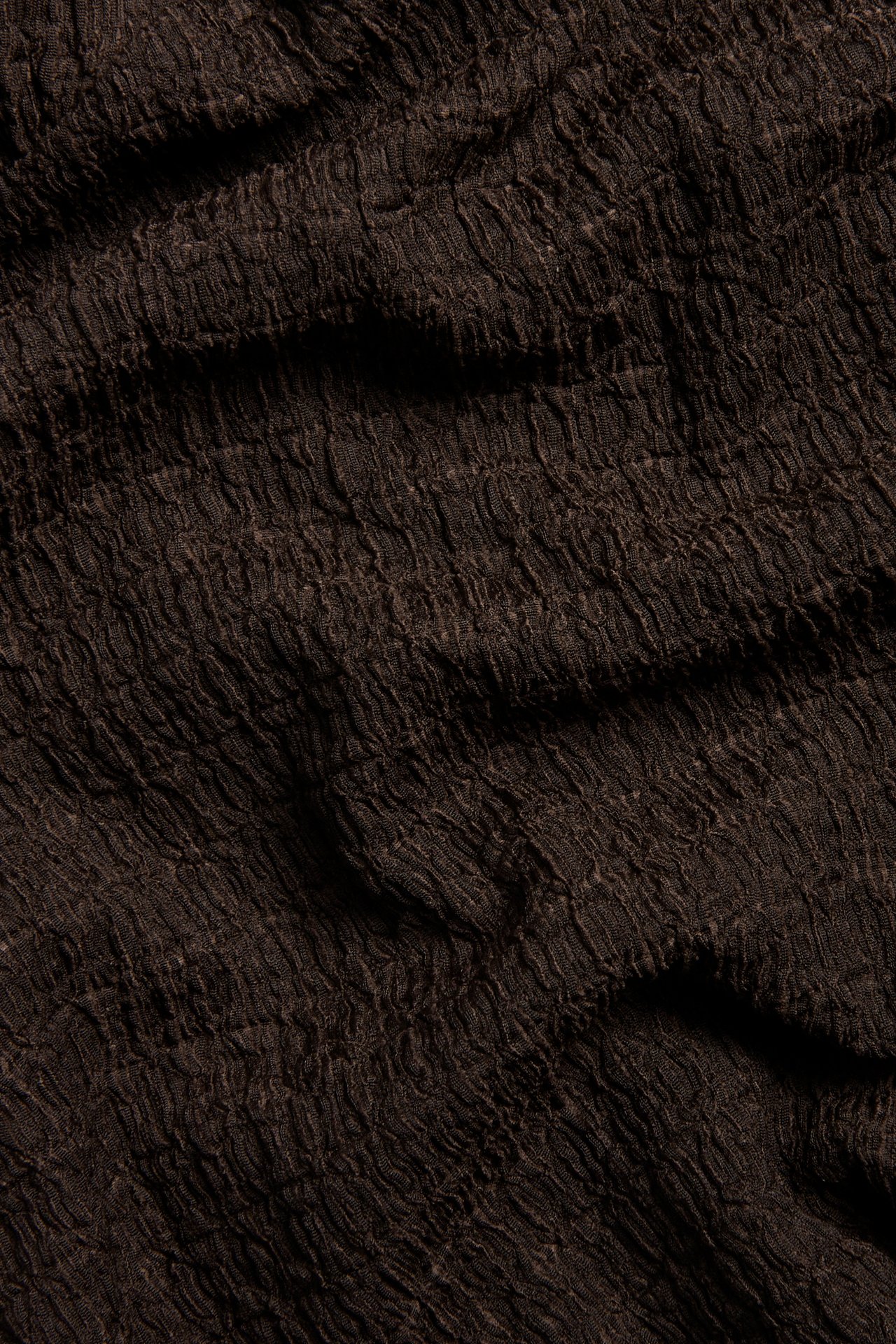 Nærbilde av mørkebrunt strukturert polyesterstoff, sannsynligvis fra en kortermet topp.