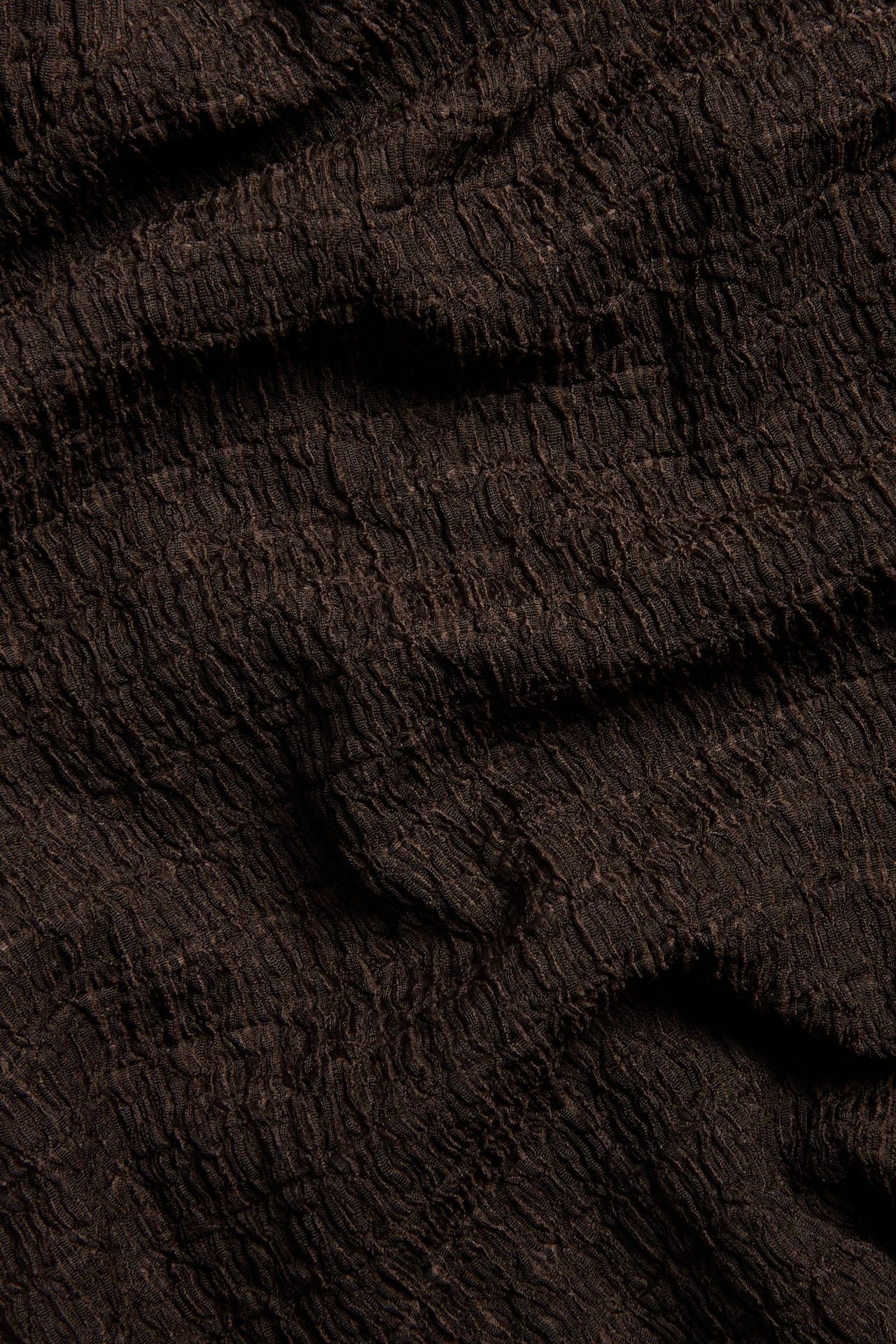 Zbliżenie na ciemnobrązowy, strukturalny materiał poliestrowy, prawdopodobnie z topu z krótkim rękawem.