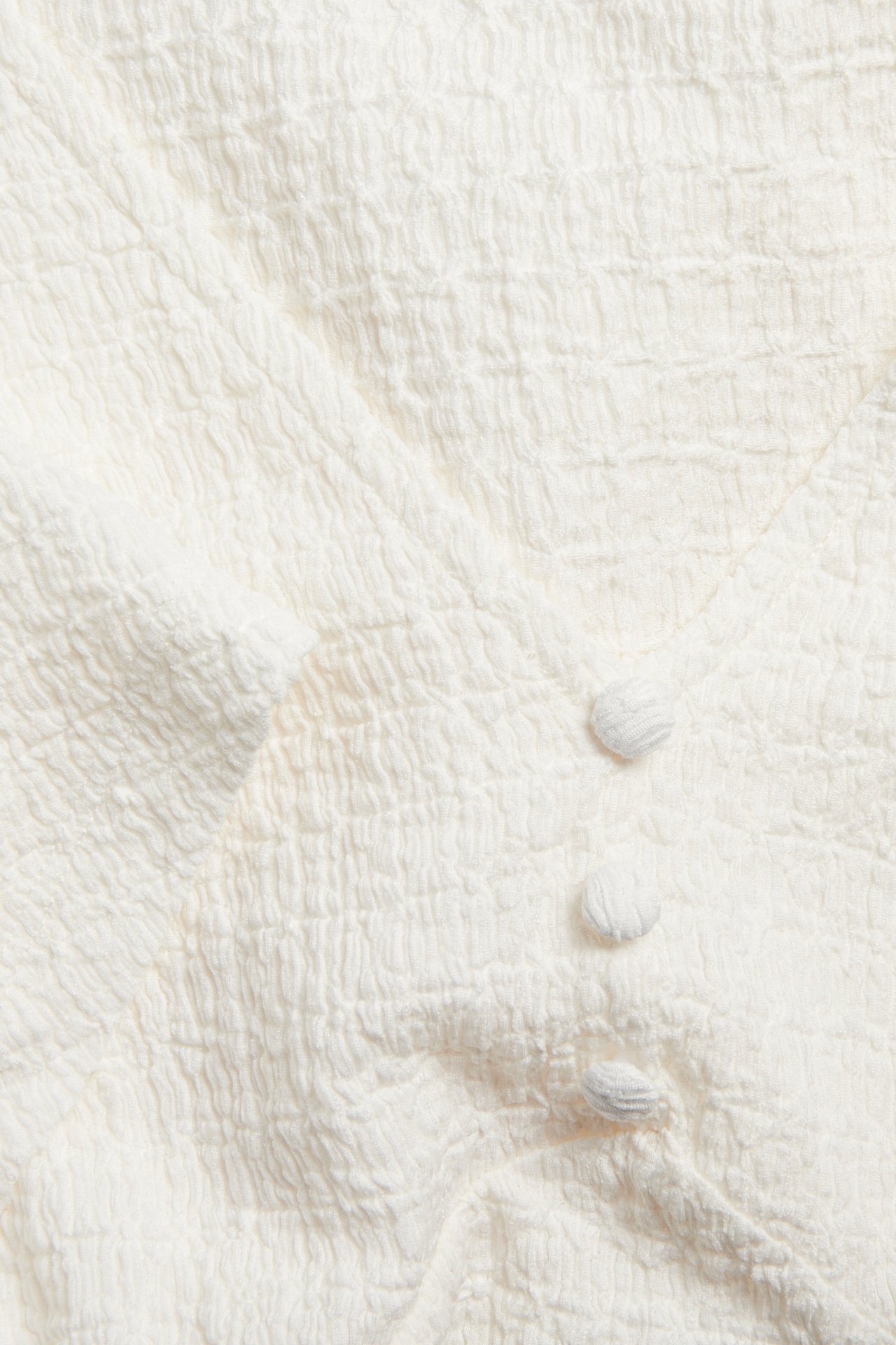 Lähikuva luonnonvalkoisesta kuviollisesta V-kaula-aukkoisesta topista kolmella kangasnapilla.