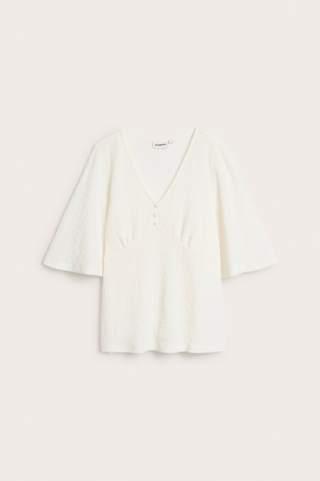 Framifrån, en offwhite, strukturerad kortärmad V-ringad topp med vida ärmar och tre knappar fram.