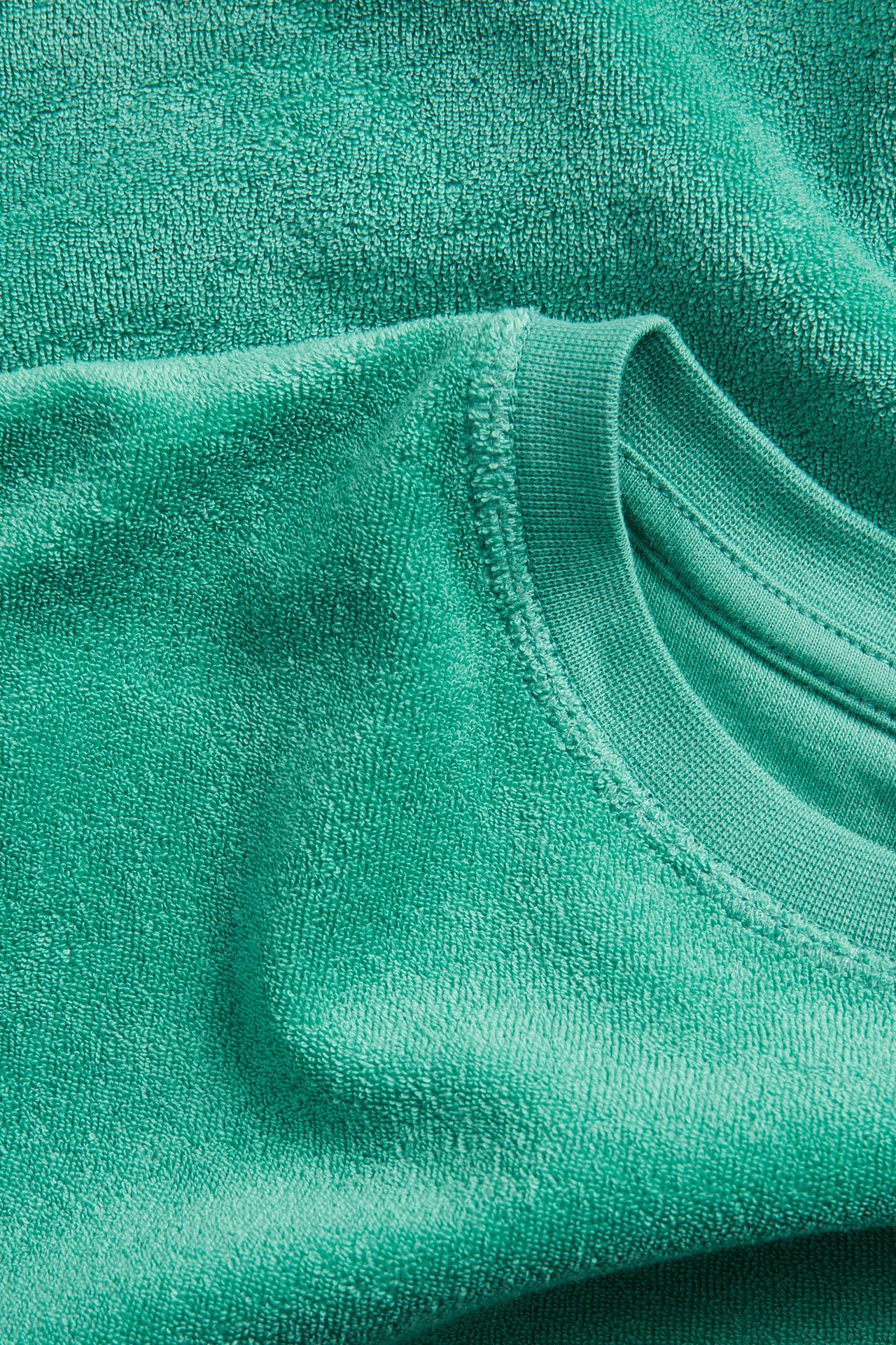 Närbild av en grön kortärmad frotté-t-shirt med ribbad rundhals, som visar dess mjuka, texturerade tyg.
