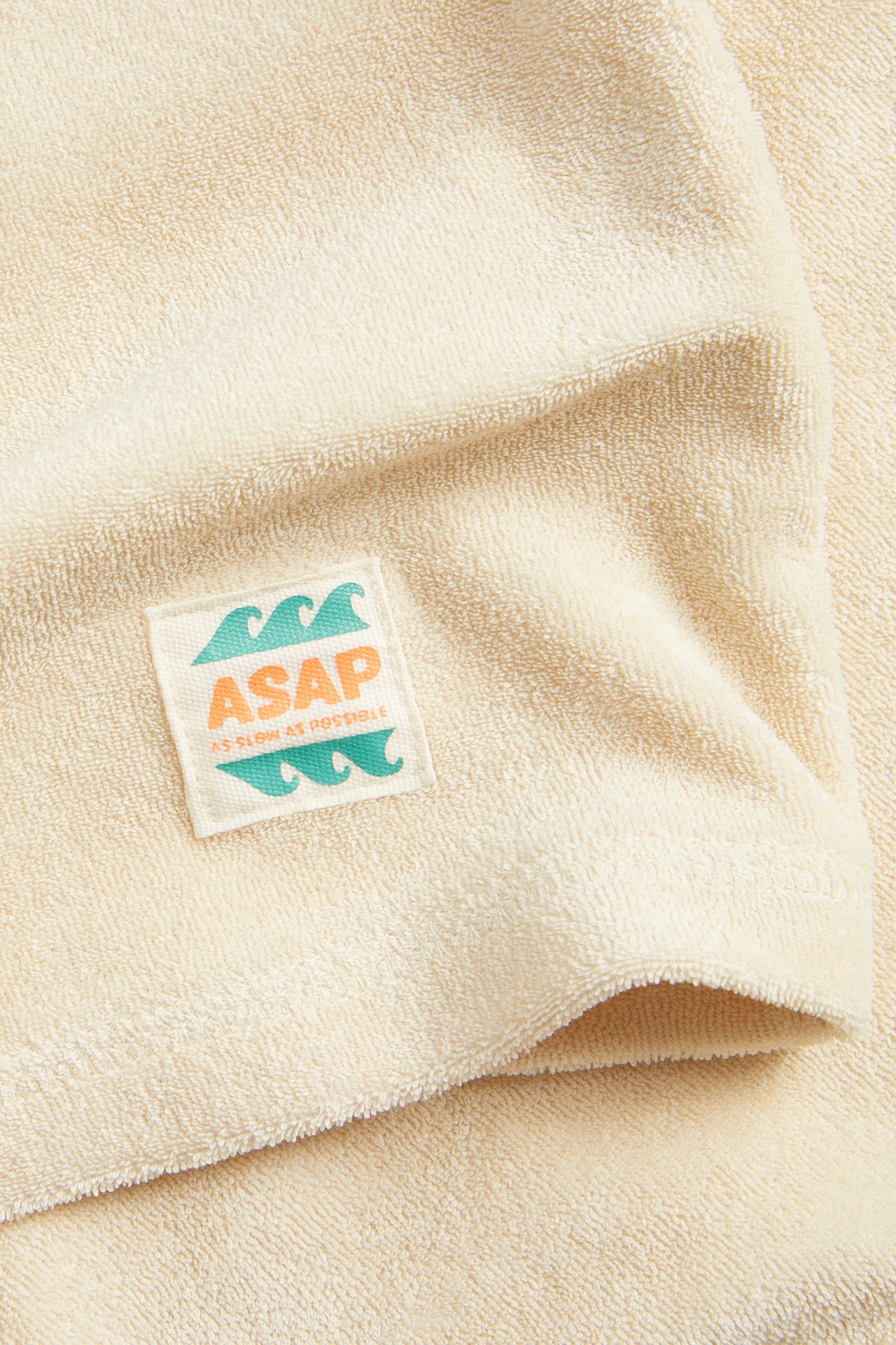 Närbild av ljusbeige frotté T-shirt med en fyrkantig "ASAP" canvaspatch.