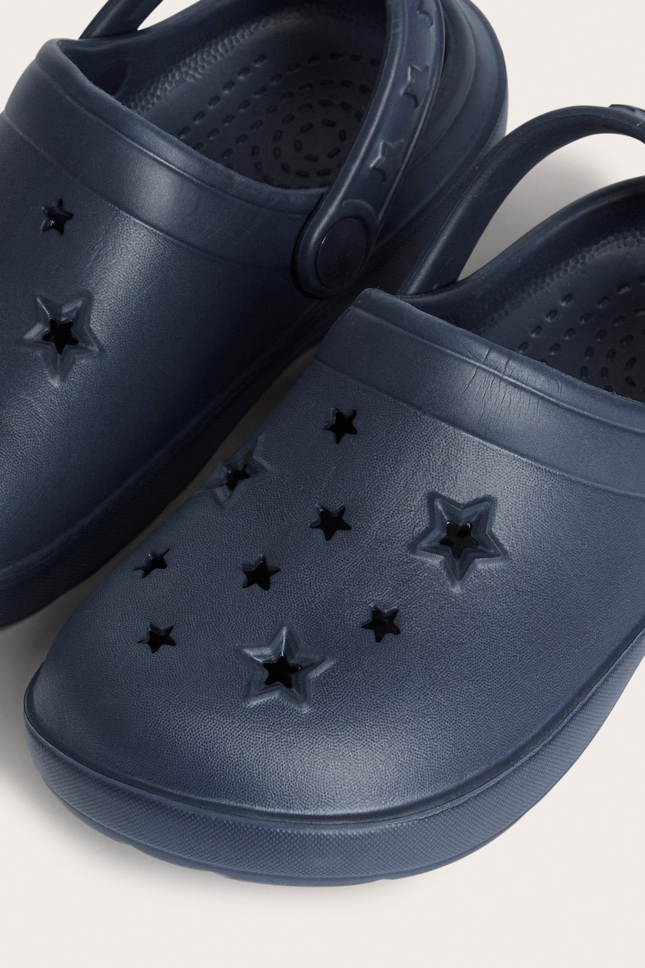 Zbliżenie na granatowe plastikowe klapki dziecięce z wycięciami w kształcie gwiazd z przodu.