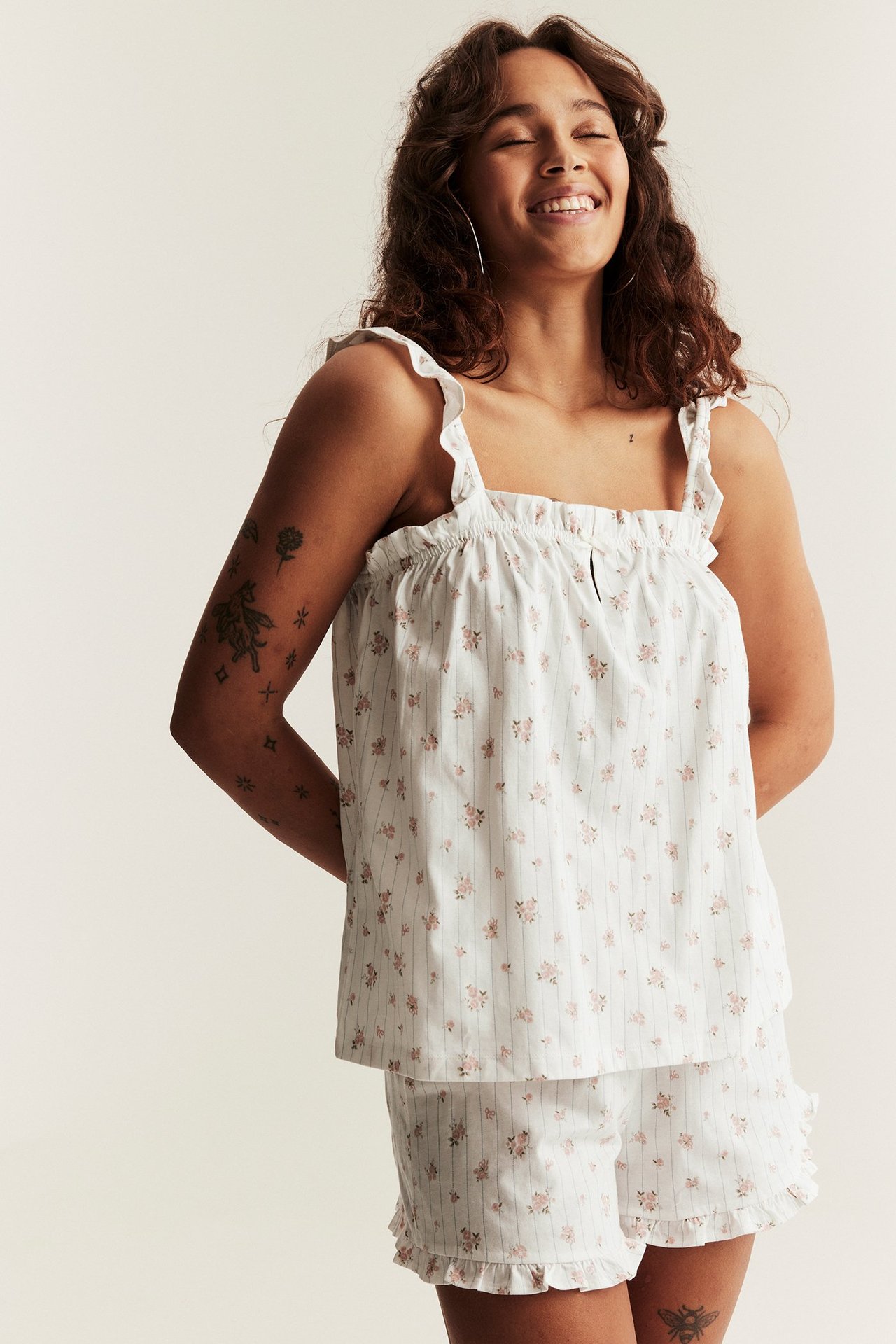 Widok z przodu uśmiechniętej kobiety w ecru bawełnianej piżamie z różowym kwiatowym wzorem w paski.