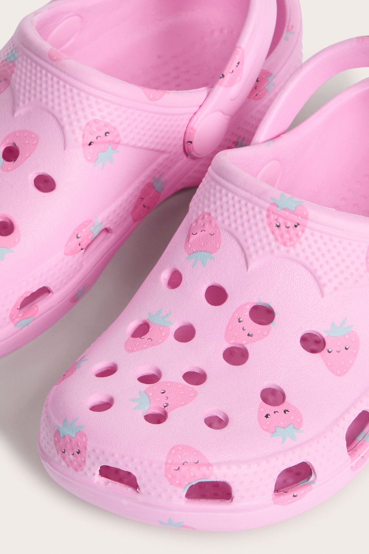 Zbliżenie na dwa jasnoróżowe plastikowe klapki z truskawkowym wzorem i otworami wentylacyjnymi.