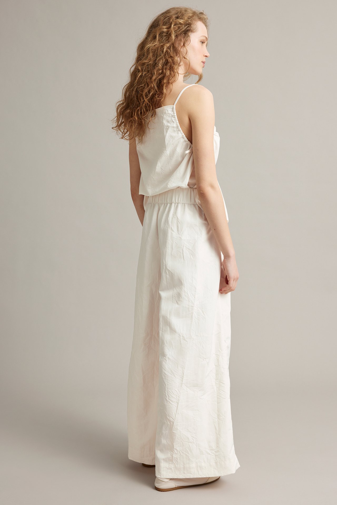 Bakifrån: Kvinna i vita vida byxor med resår i midjan och struktur, samt matchande linne.