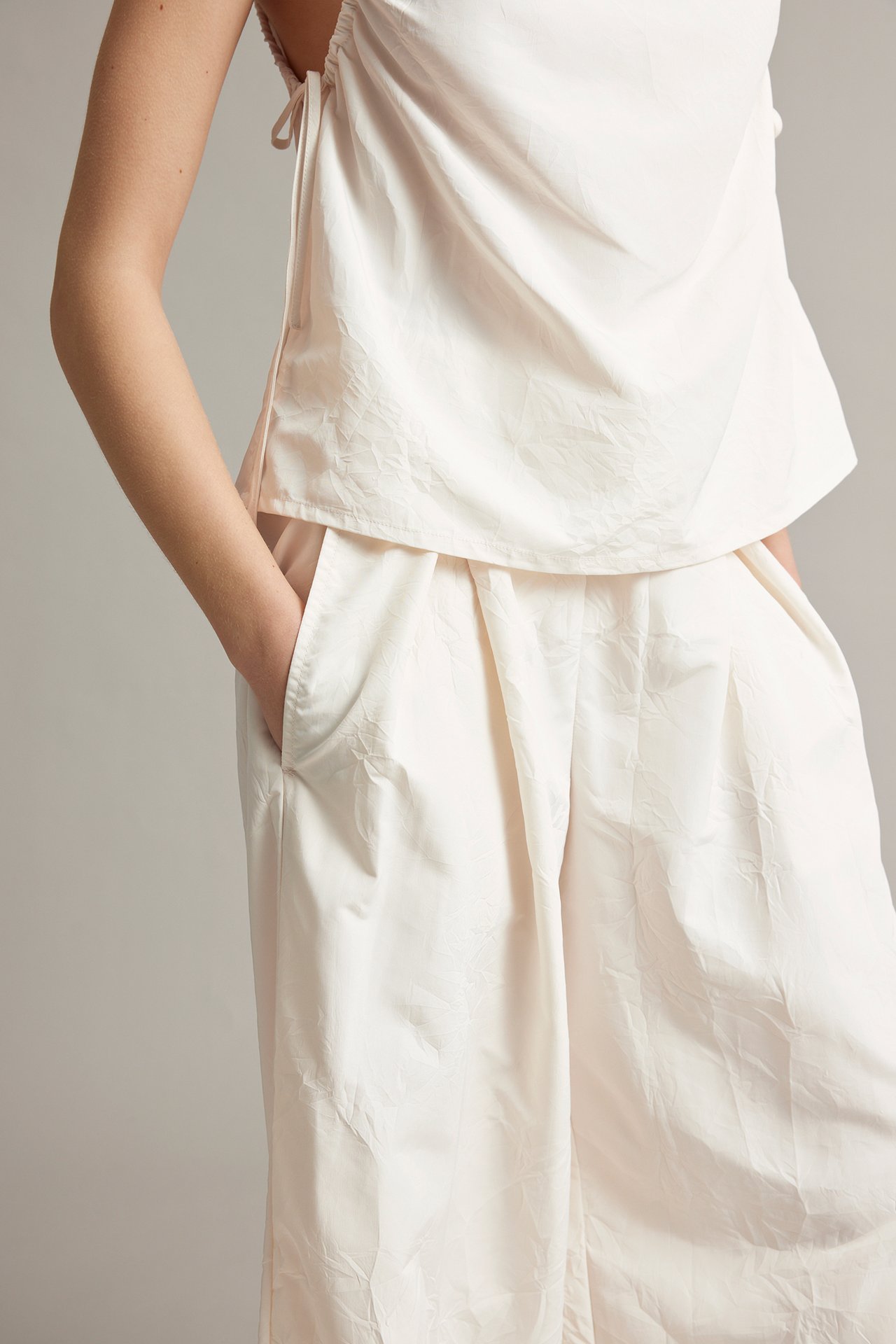 Närbild framifrån på en kvinna i vita vida byxor med struktur, veck fram och sidfickor.