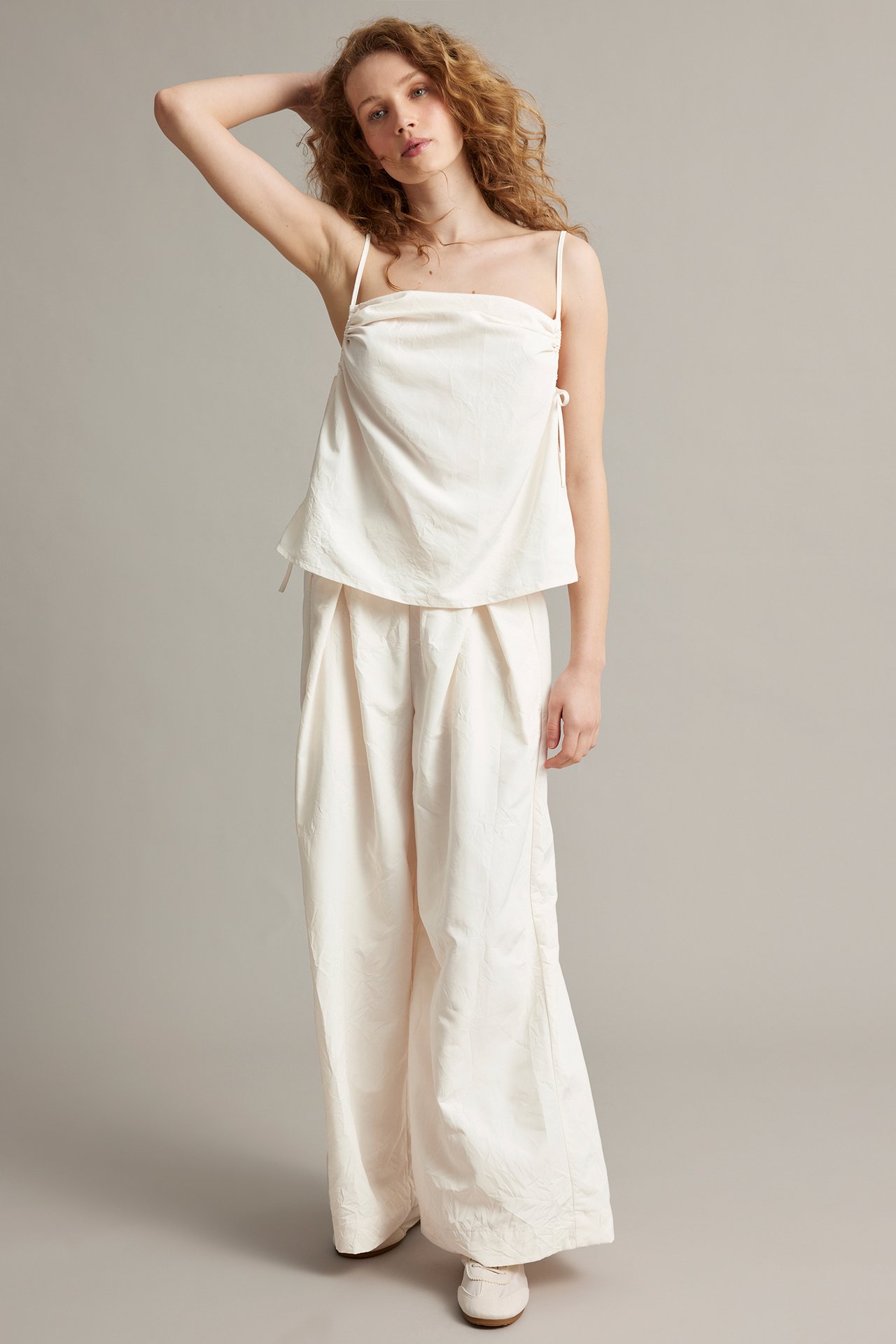 Kobieta przodem w białych szerokich spodniach z zakładkami i białym topie na ramiączkach.