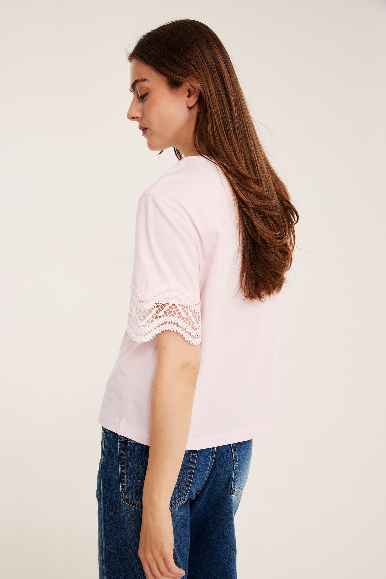 Sidovy av en kvinna i en lös ljusrosa t-shirt med spetsärmar och blå jeans.