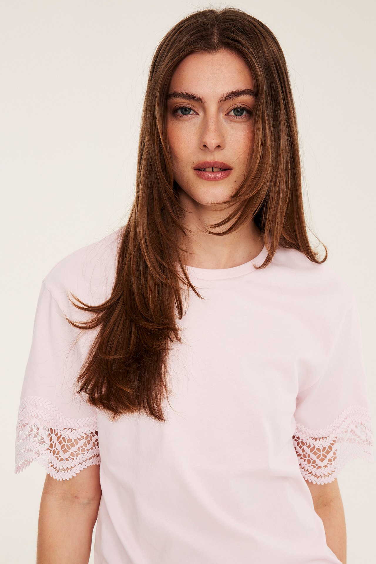 Från framsidan, en kvinna i en lös ljusrosa t-shirt med korta spetsärmar.