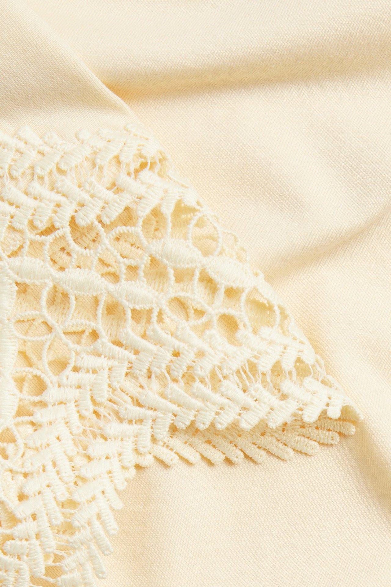 Nærbilde av en lys gul løs T-skjorte-erme med intrikat blondemønster.