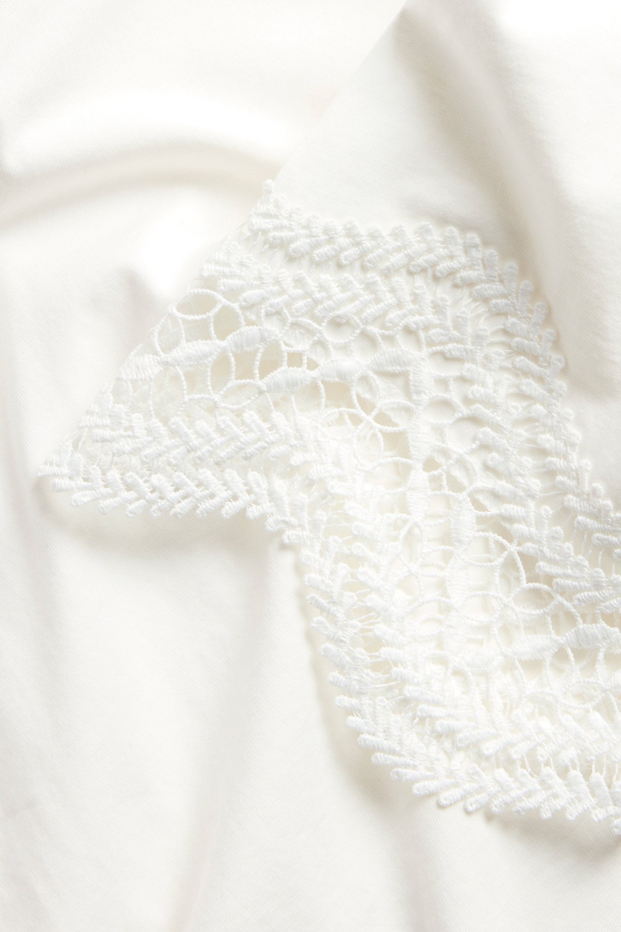 Lähikuva luonnonvalkoisesta t-paidasta, jossa on yksityiskohtainen valkoinen pitsikoriste.