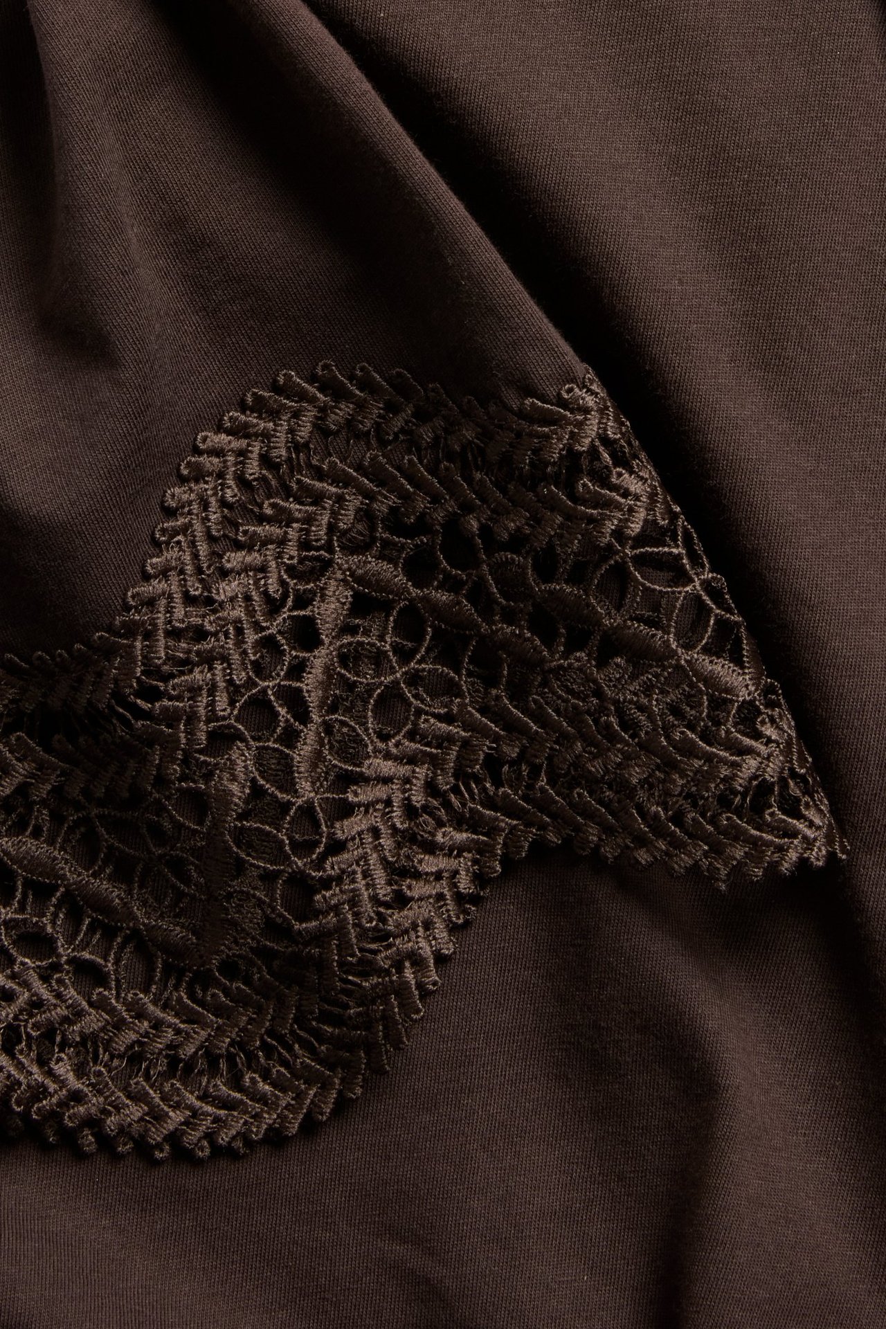 Zbliżenie ciemnobrązowego, luźnego T-shirtu z koronkowymi rękawami.