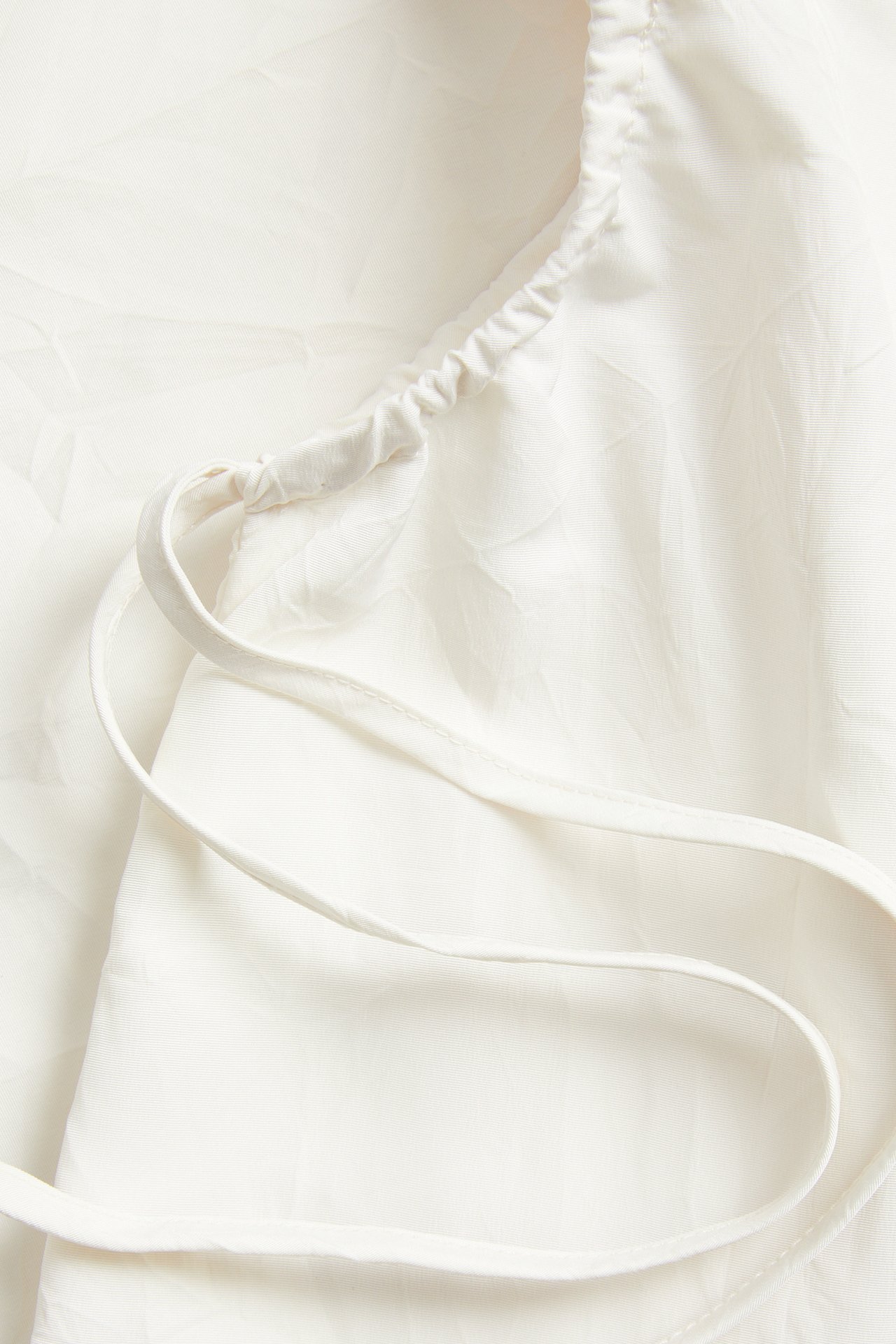 Nærbilde av en hvit polyestertopp med rynket overkant og tynne, justerbare skulderstropper.