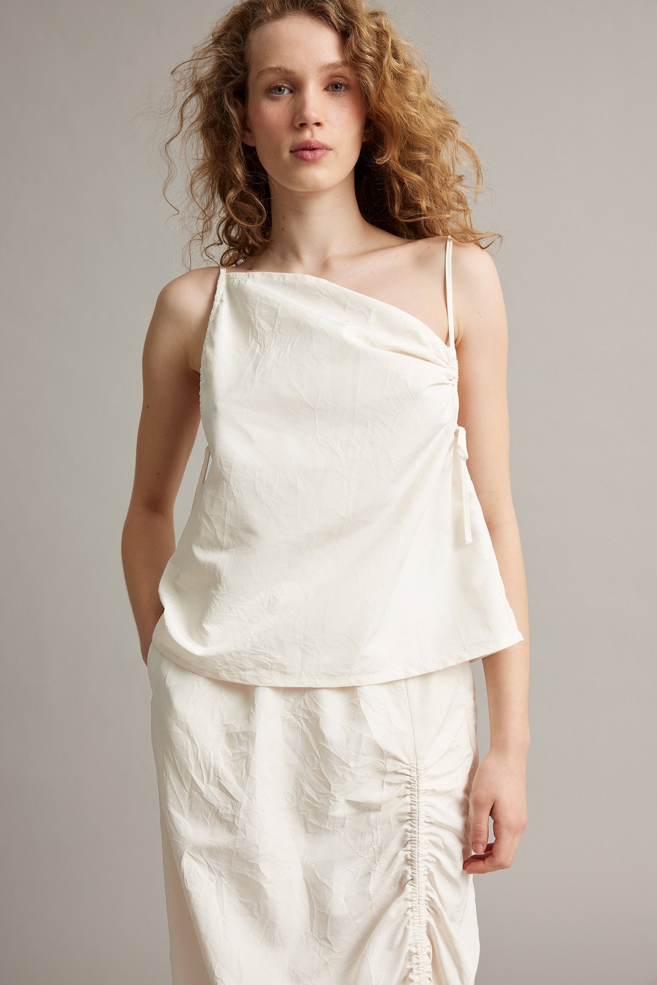 Widok z przodu: kobieta w białym, strukturalnym, drapowanym topie na ramiączkach i pasującej marszczonej spódnicy.