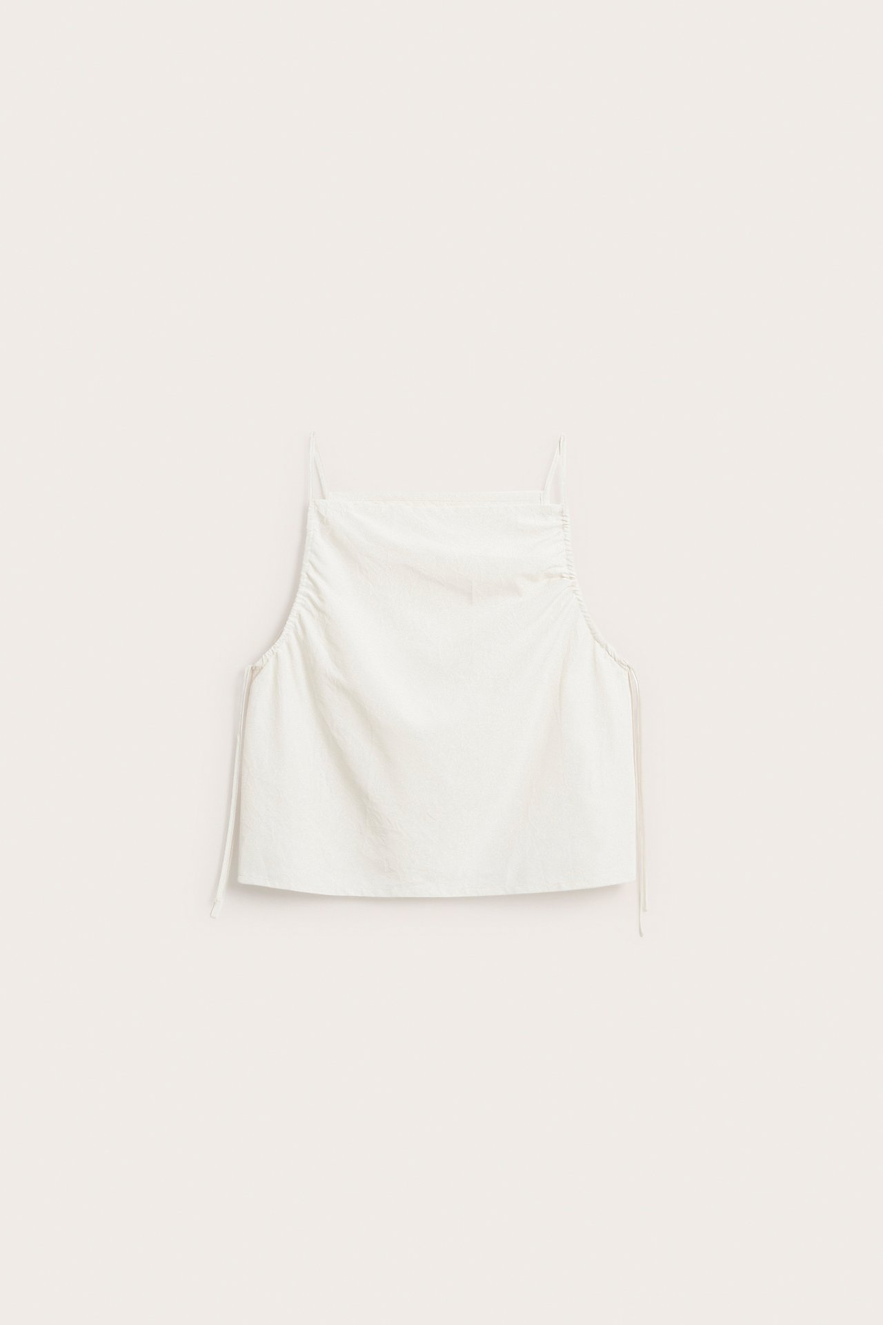 Frontutsikt av en hvit polyestertopp med justerbare stropper og draperte detaljer.