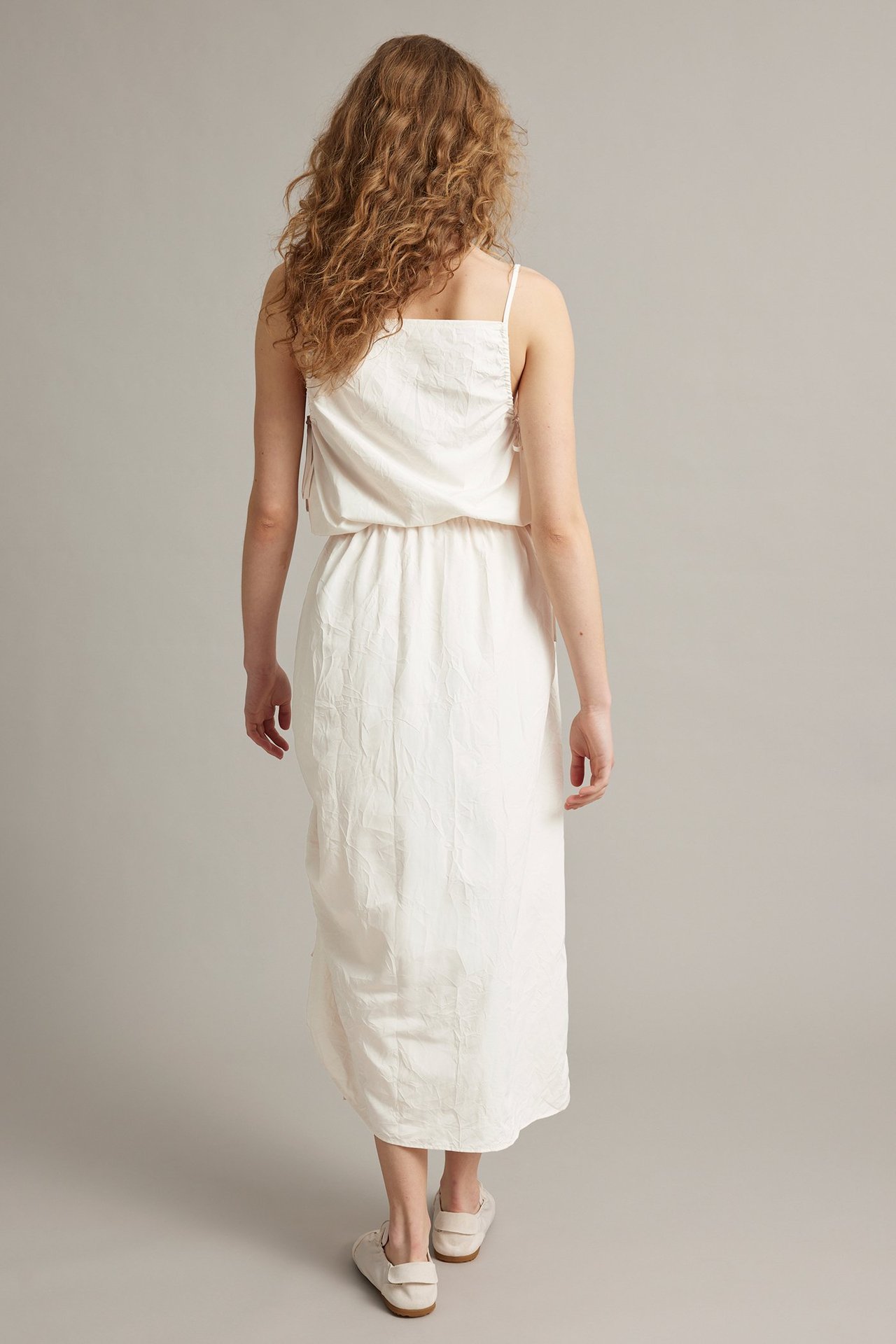 Takaa: nainen valkoisessa polyesteri midihameessa, jossa sivudrapeeaus, joustovyötärö ja yhteensopiva toppi.