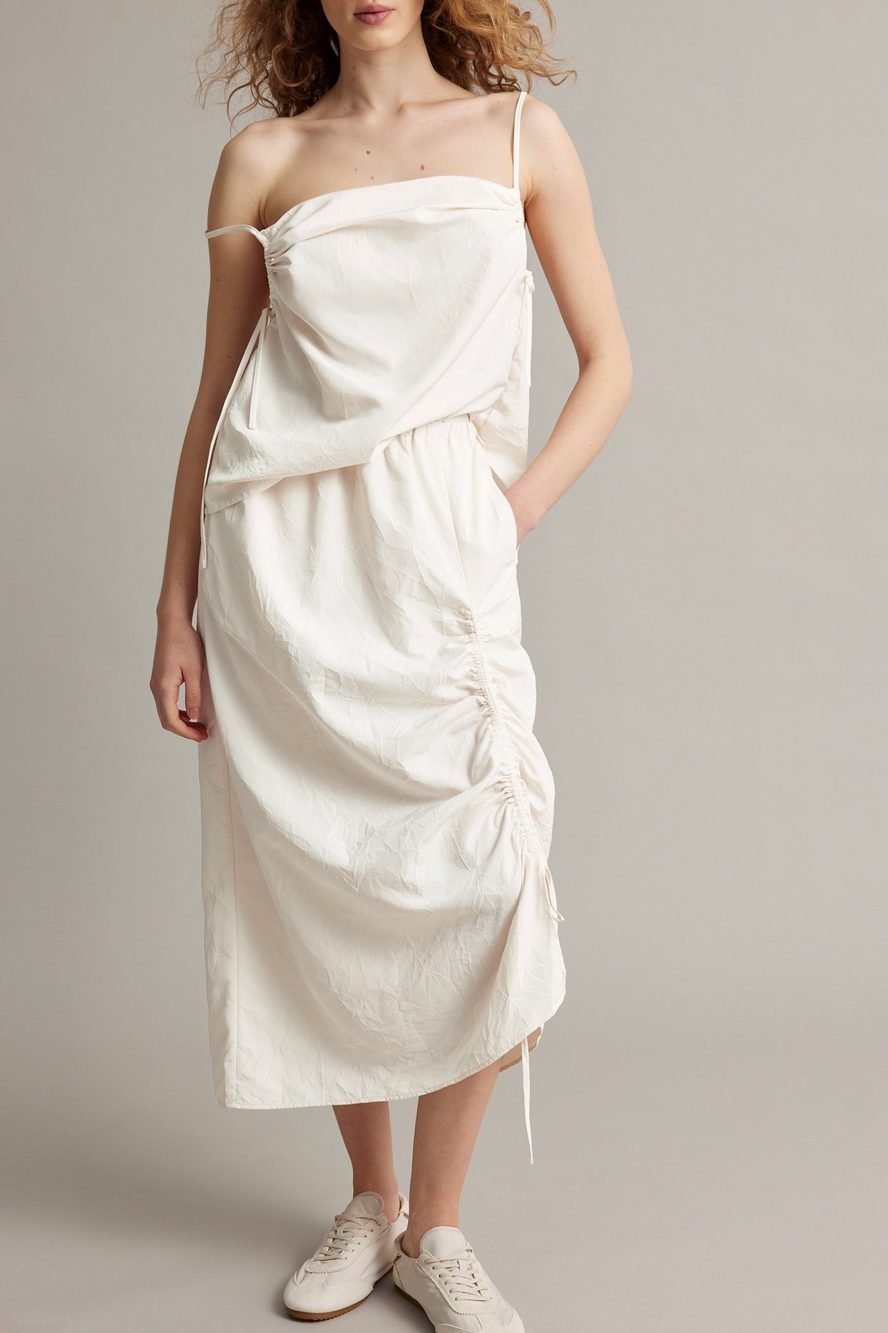 Edestä: Nainen valkoisessa rypytetyssä midihameessa, yhteensopivassa olkaimettomassa topissa ja valkoisissa lenkkareissa.