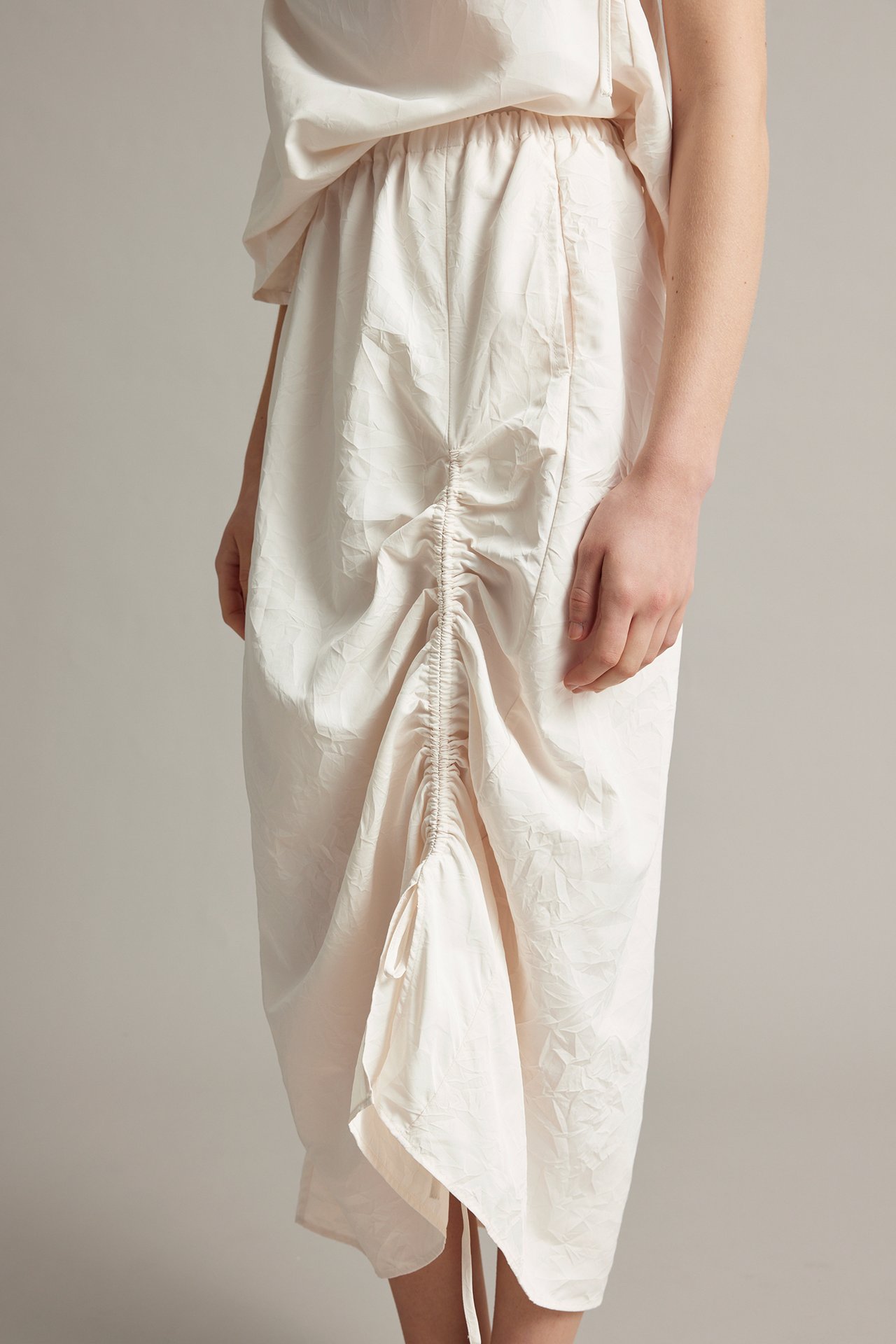 Edestä: Nainen valkoisessa rypytetyssä hameessa, joustava vyötärö ja yhteensopiva toppi.