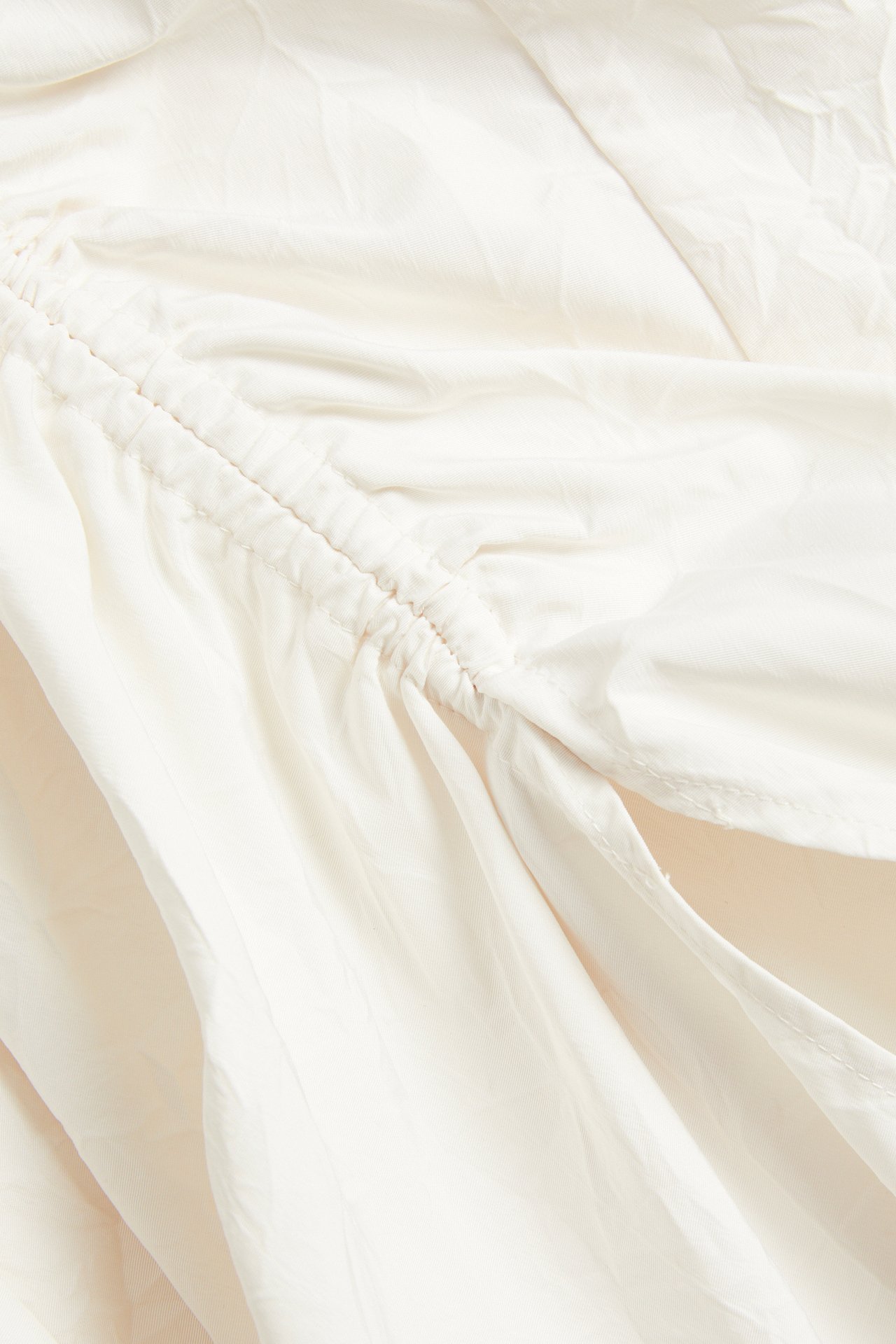 Nærbilde av et hvitt polyesterskjørt med rynkede detaljer langs en sidekanal.