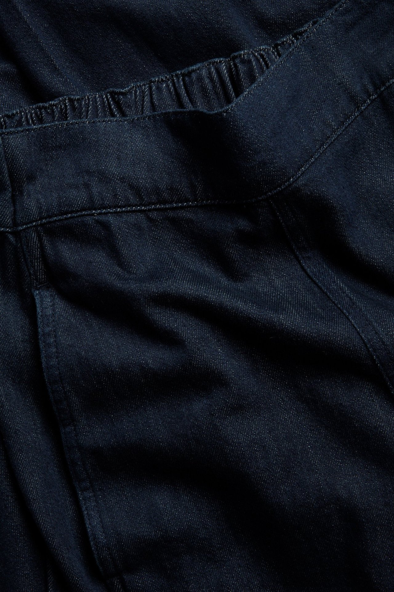 Zbliżenie ciemnych dżinsów pull-on z elastyczną talią i widocznymi szwami.