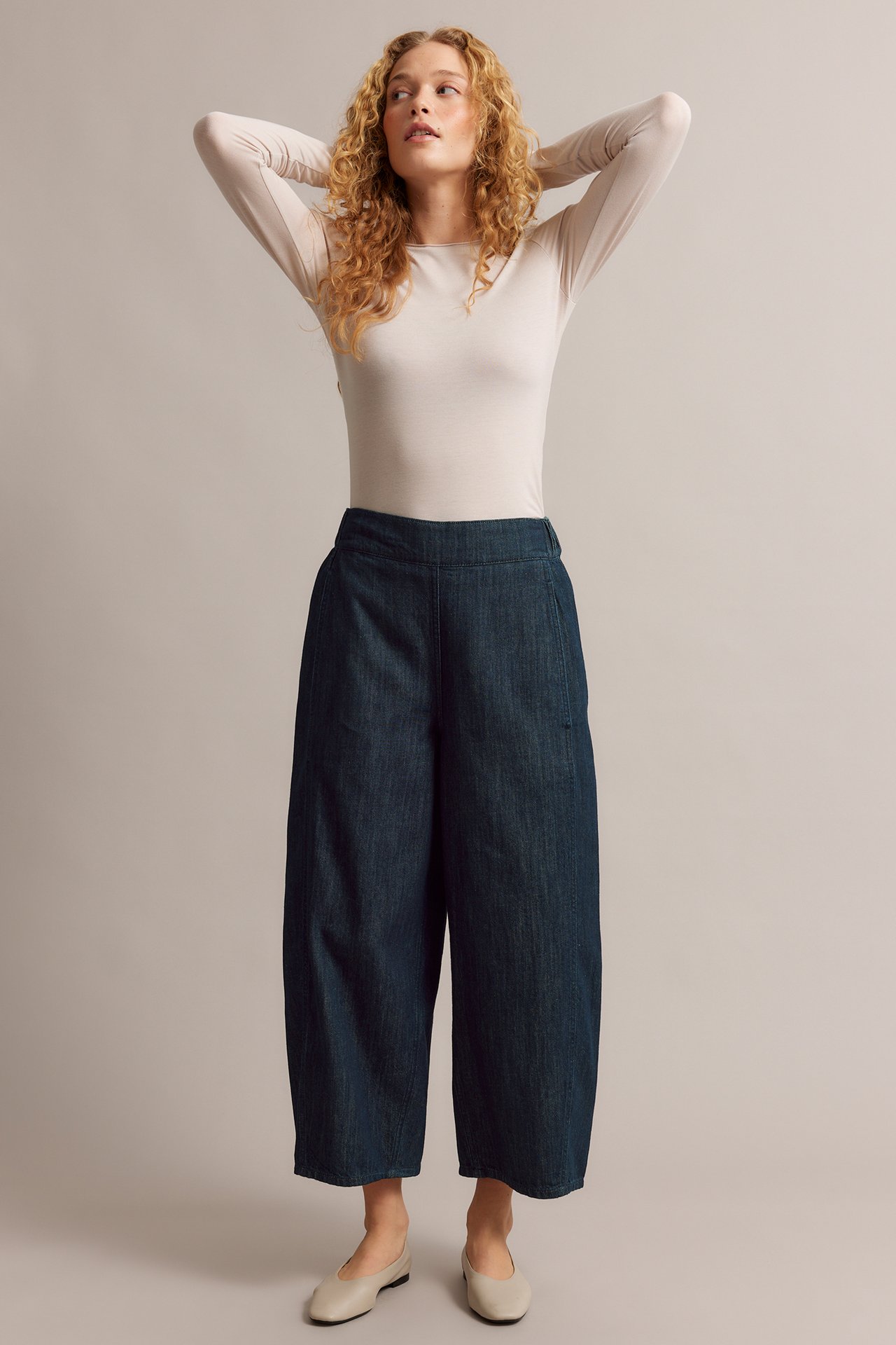 Edestä: nainen tummansinisissä barrel leg -pull-on-farkuissa, vaalea pitkähihainen toppi ja beiget avokkaat.