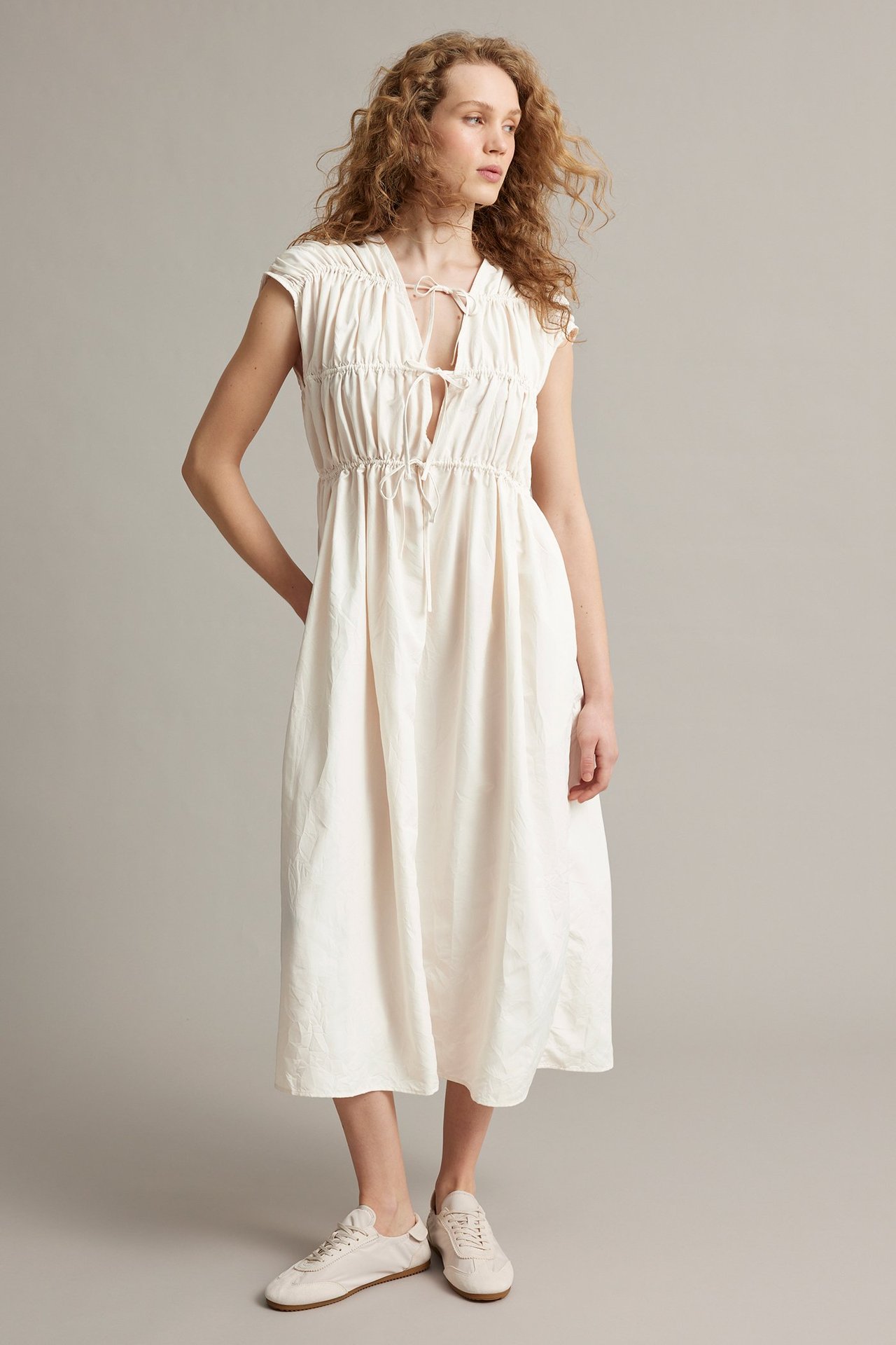 Framifrån: Kvinna i vit midiklänning med knytdetaljer och ljusa sneakers.